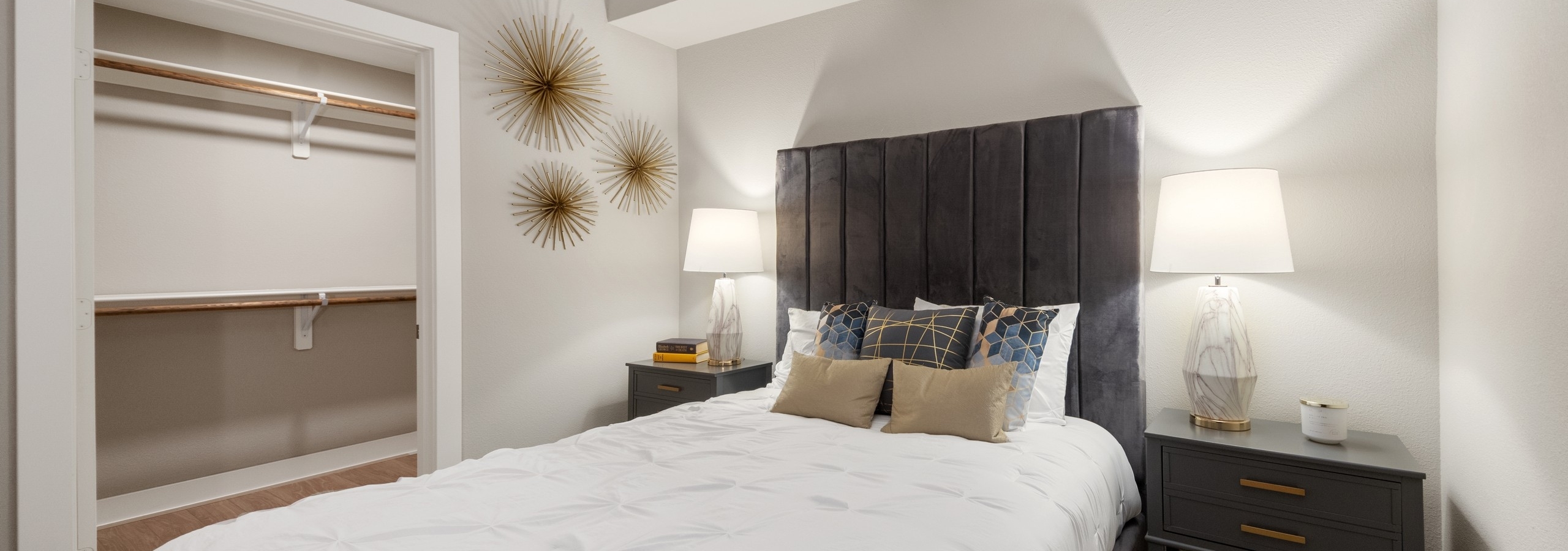 AMLI Riverfront Green apartment bedroom featuring a white bedspread and geometric decor with view into walk in closet