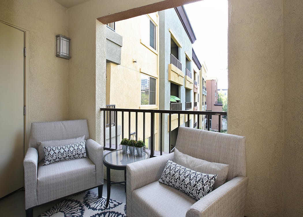 Daytime view of a private patio with area rug, cushioned lounge chairs and accent pillows at AMLI Warner Center apartments