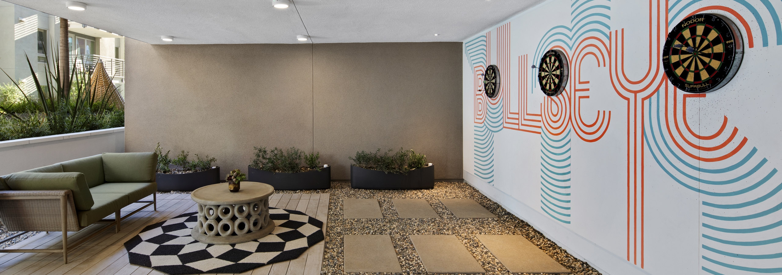 Daytime view of outdoor courtyard cave with round checkered rug and three dartboards on wall at AMLI Park Broadway apartments