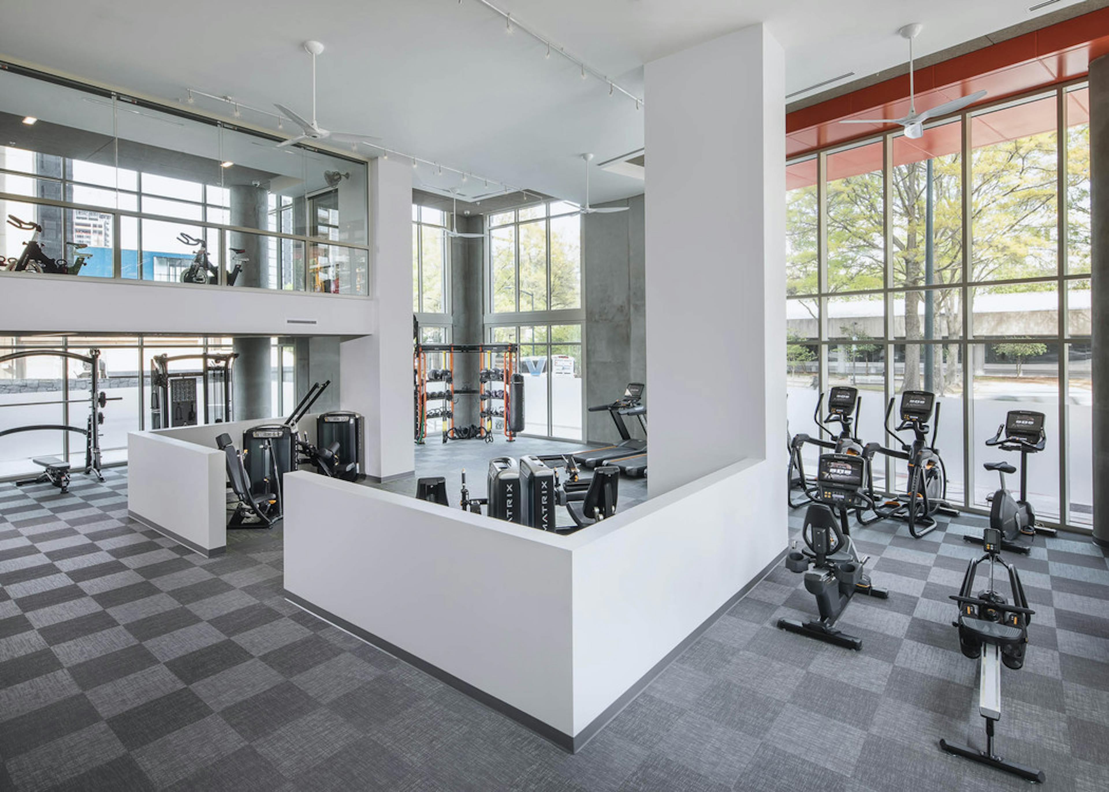 AMLI Arts Center fitness center with checkered flooring and a variety of exercise machines facing floor to ceiling windows