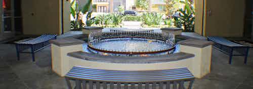 Exterior daytime view of AMLI Warner Center apartment wishing well-style fountain with surrounding benches and lush greenery