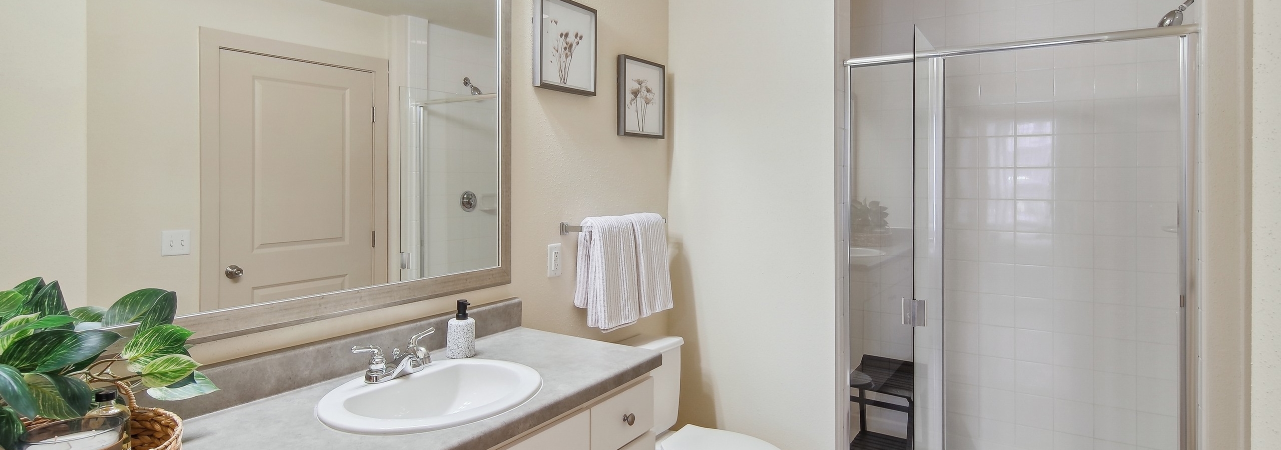 Bathroom at AMLI Park Avenue with a white tile shower with a sink with a large mirror and hardwood flooring