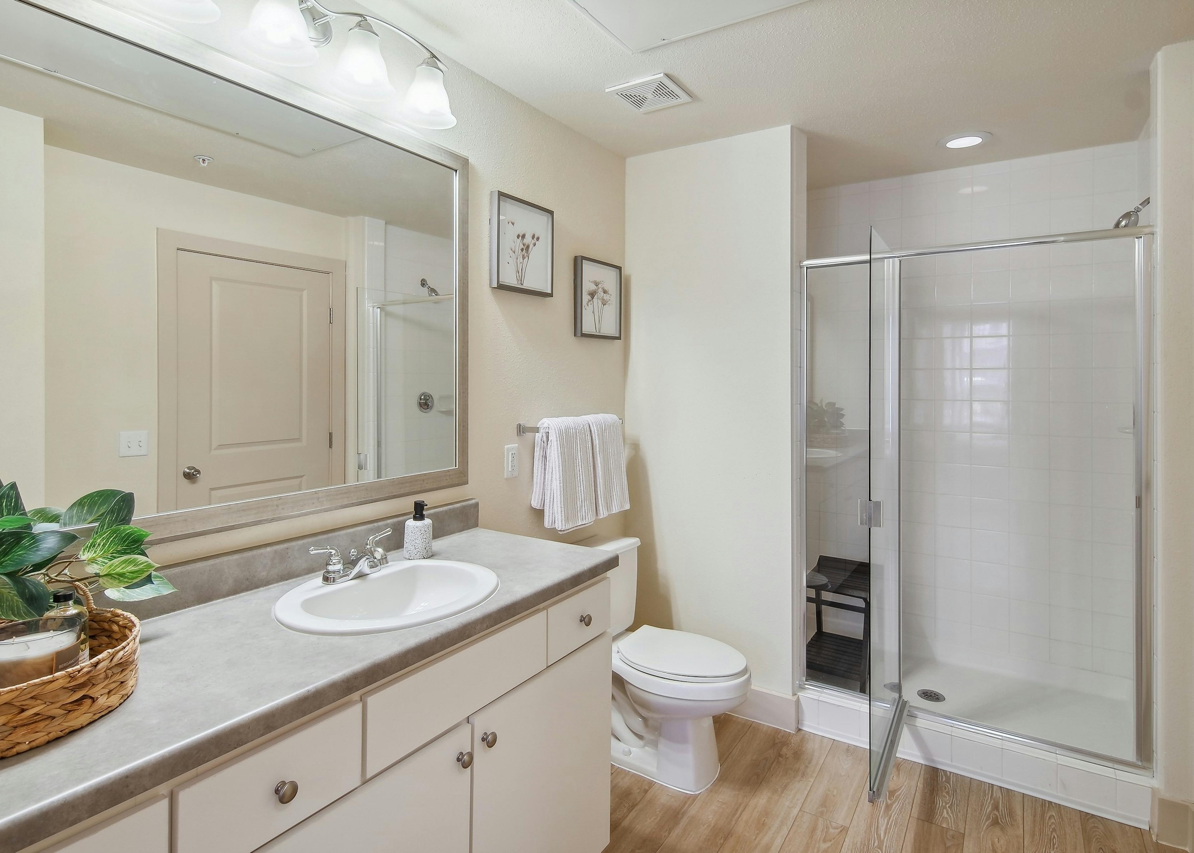Bathroom at AMLI Park Avenue with a white tile shower with a sink with a large mirror and hardwood flooring