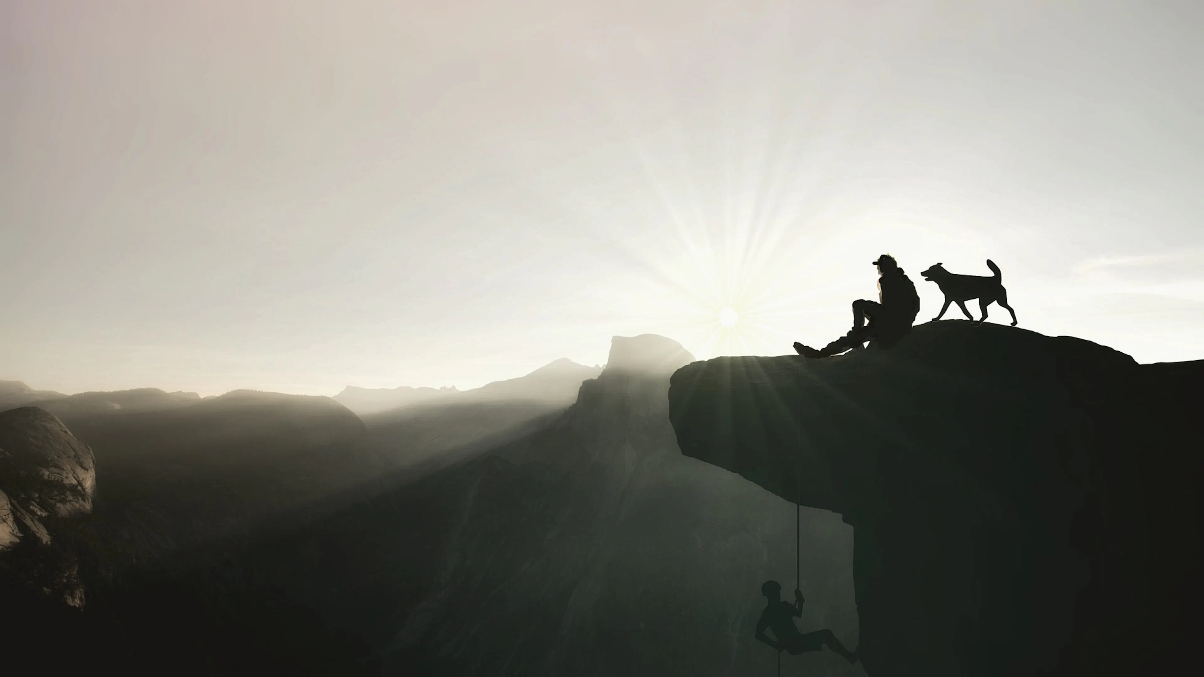 Man with dog on cliff overlooking mountains with man climbing below