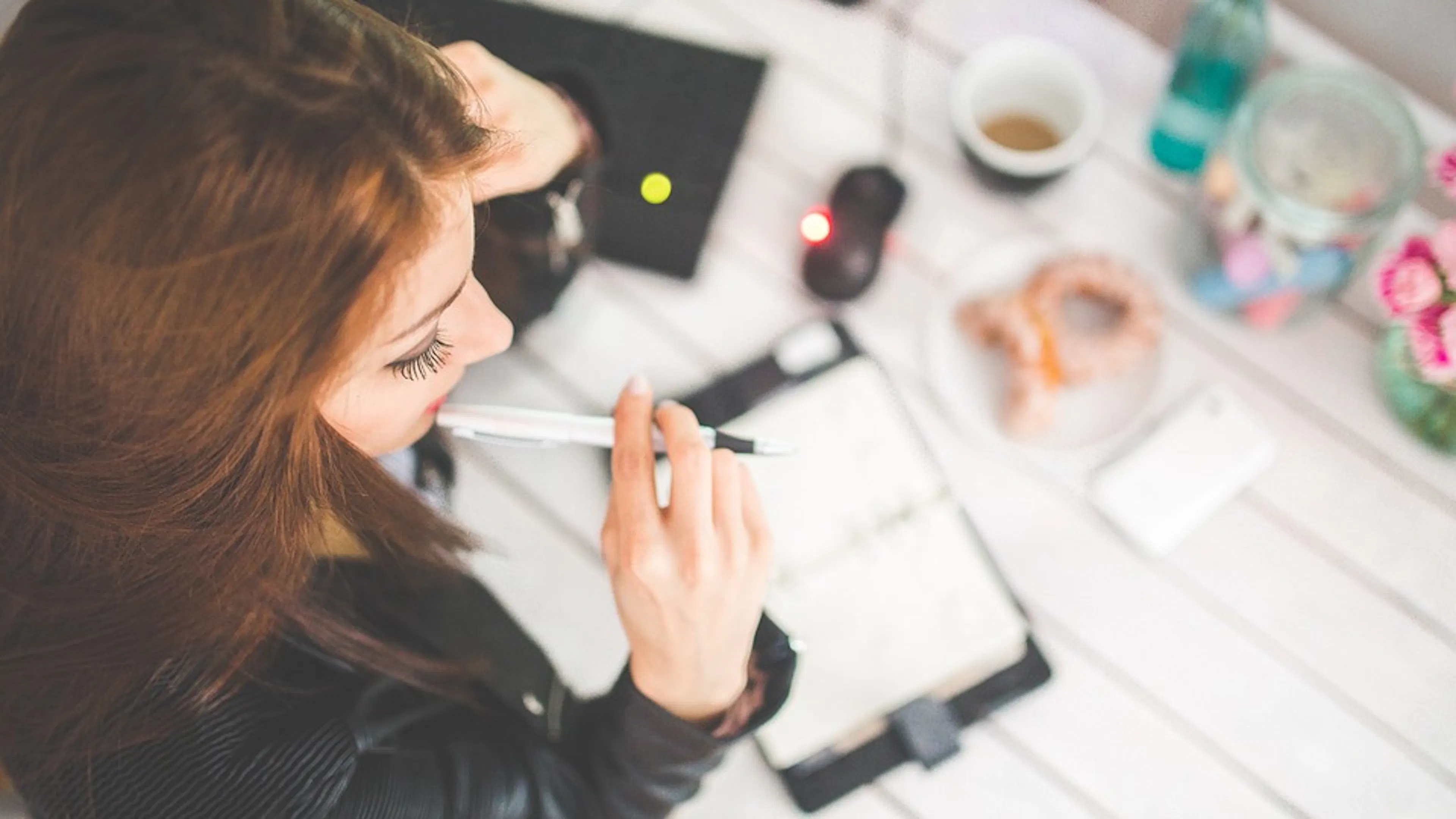 A woman working at a desk scattered with stationary and coffee cups
