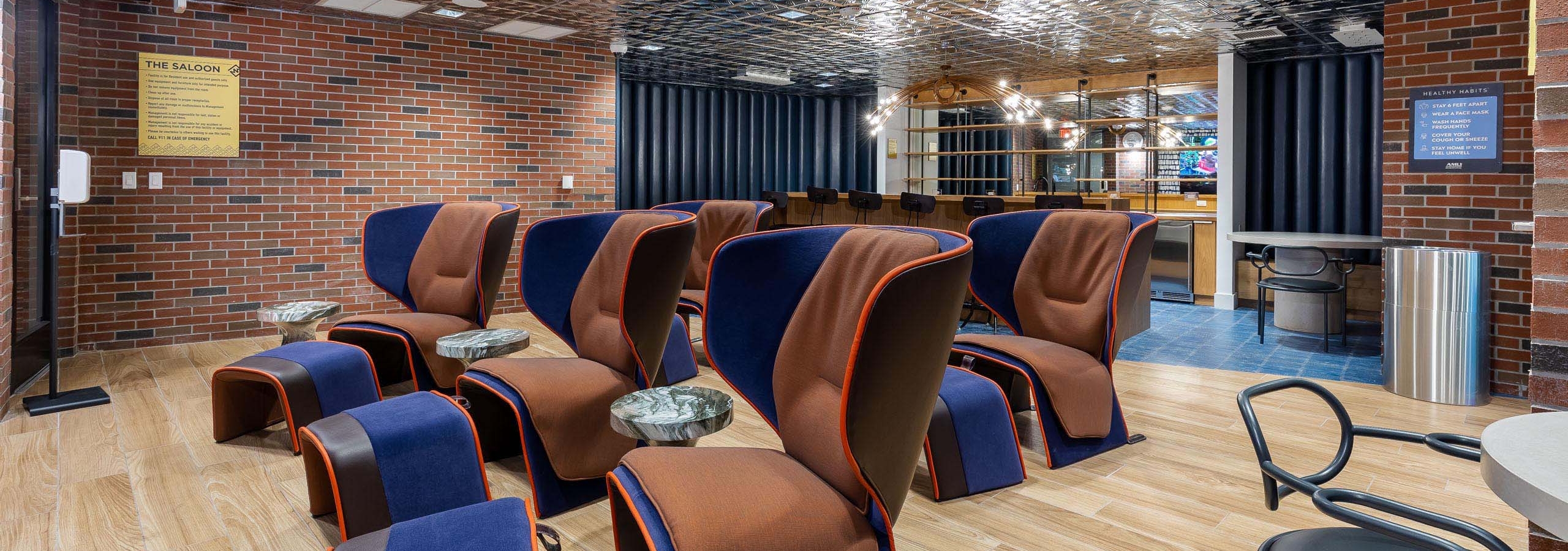 AMLI Midtown Miami theater room with large brown chairs and ottomans and wood floor with brick walls and silver ceiling
