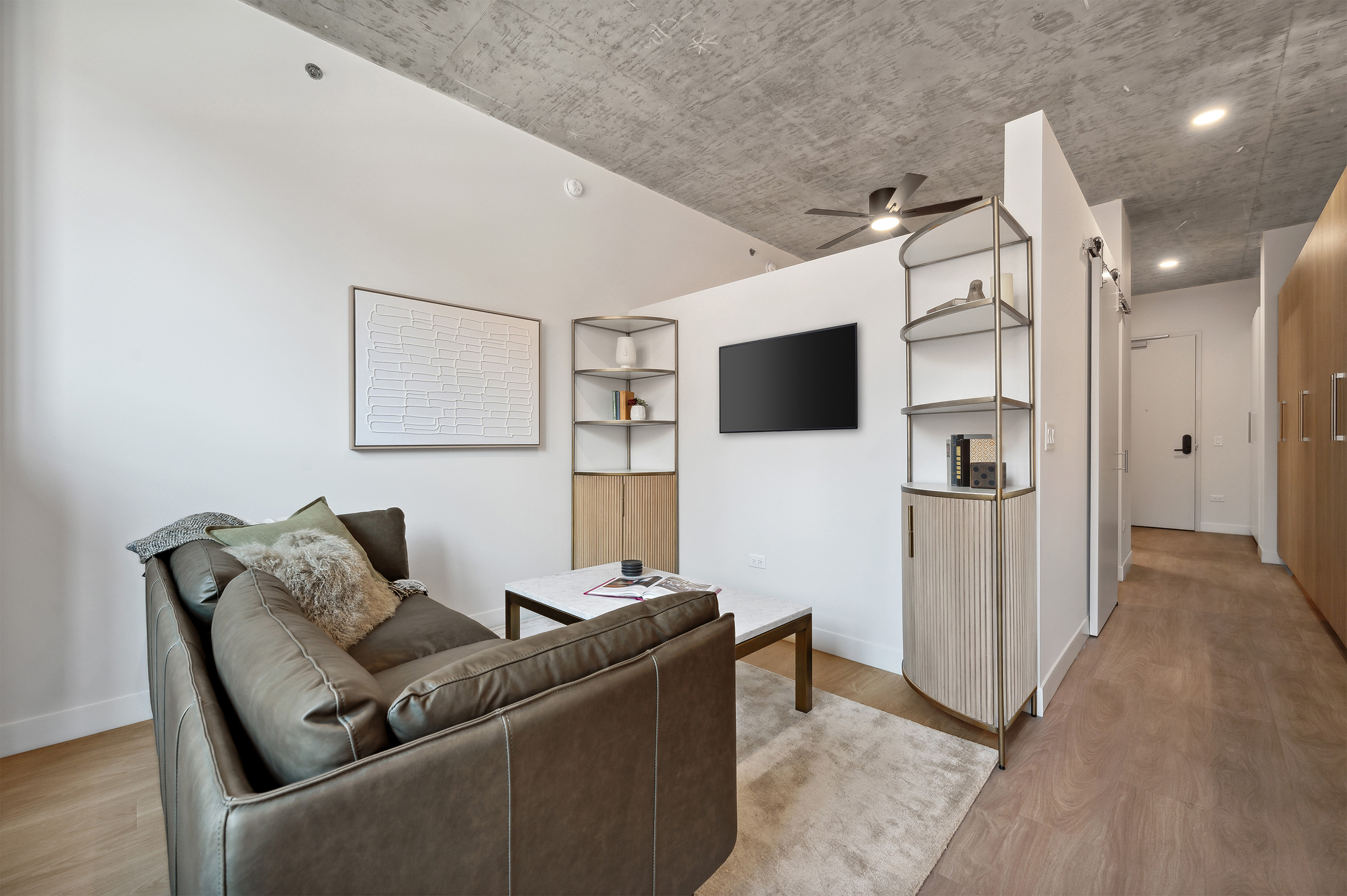Living room with grey couch and metal finish corner shelves and three quarter wall to bedroom at AMLI 808