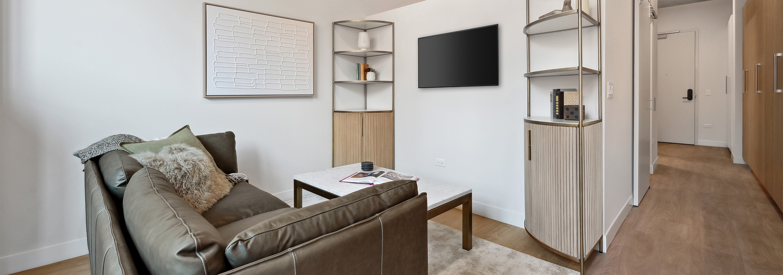 Living room with grey couch and metal finish corner shelves and three quarter wall to bedroom at AMLI 808
