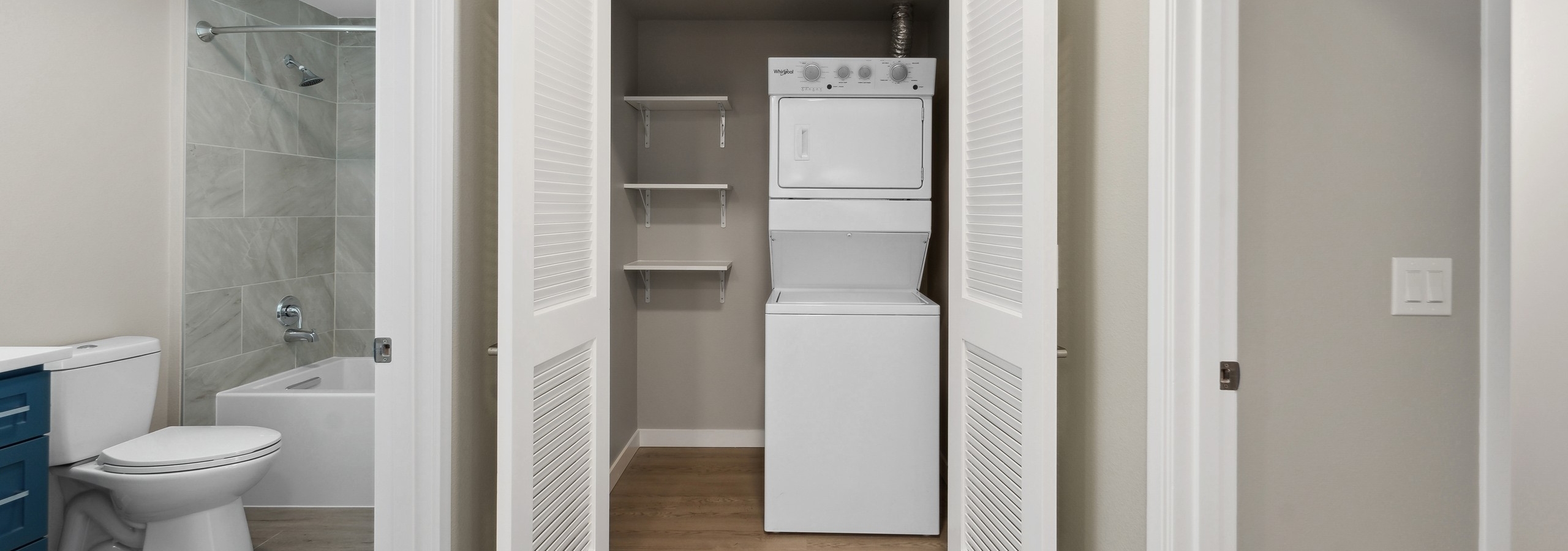 Laundry closet at AMLI 535 with a stacked white washer and dryer and shelves to the left and view into the bathroom