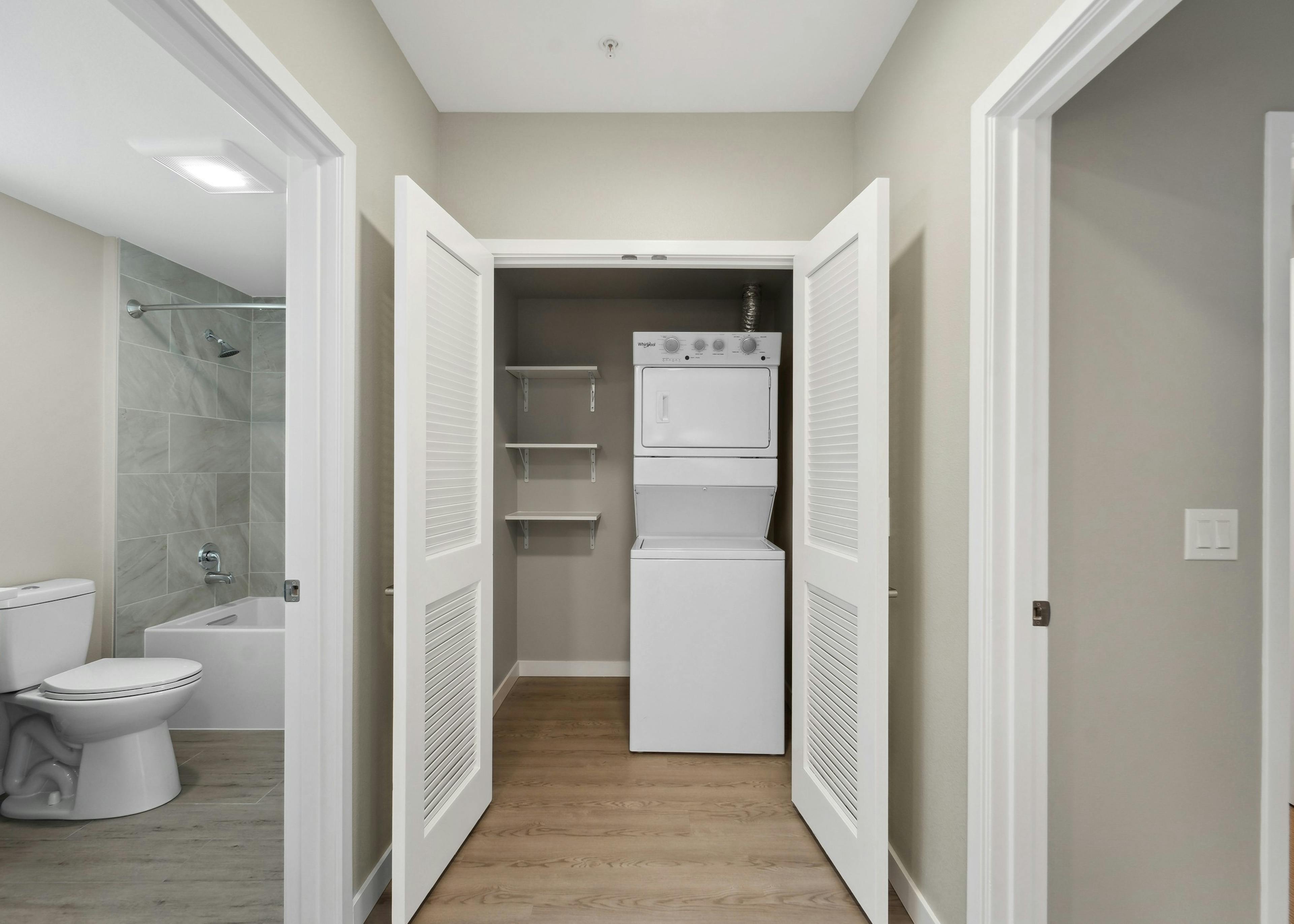 Laundry closet at AMLI 535 with a stacked white washer and dryer and shelves to the left and view into the bathroom 