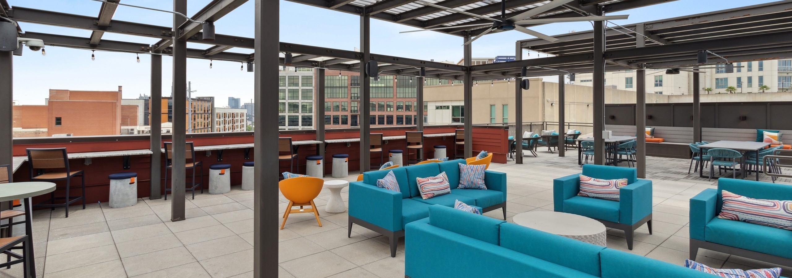 Daytime view of spacious AMLI Westside apartments rooftop with steel frame ceiling and blue couches and chairs and building views