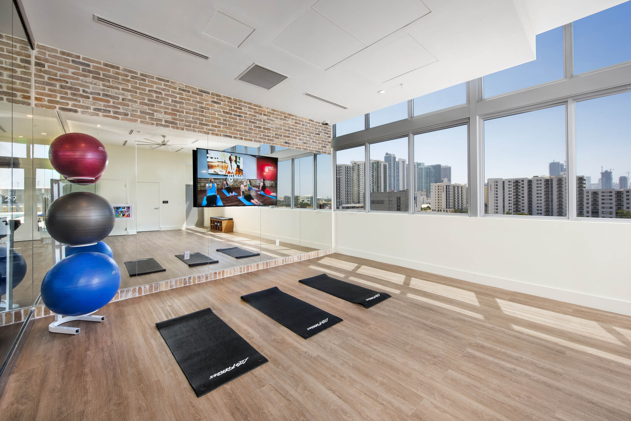 Yoga room at AMLI Midtown 29 with view of skyline and wood floors and colorful stability balls in front of mirror wall with TV