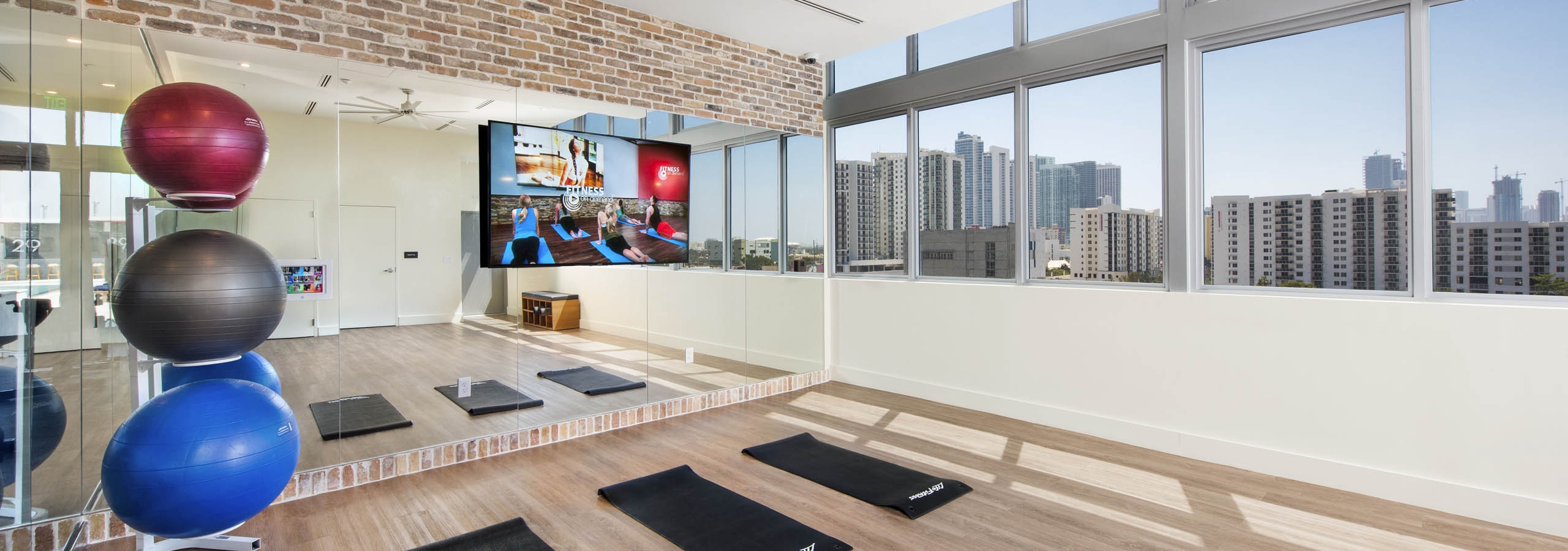 Yoga room at AMLI Midtown 29 with view of skyline and wood floors and colorful stability balls in front of mirror wall with TV