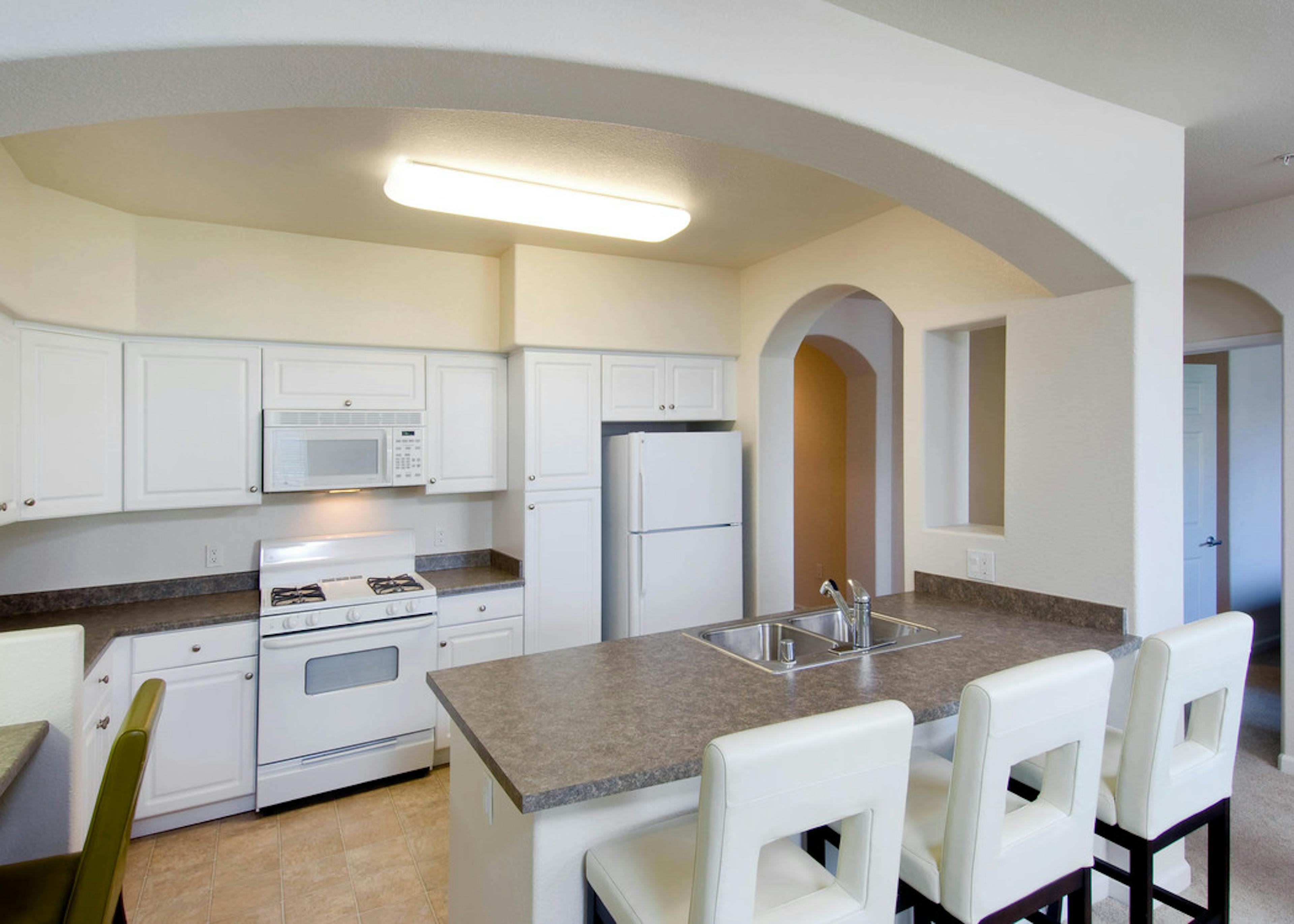 Interior view of AMLI Warner Center vacant apartment kitchen with white cabinetry and white appliances and white bar stools