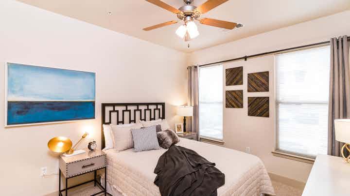 Interior view of a bedroom at AMLI Inverness with a bed with black metal headboard and a blue painting on the wall and lamps