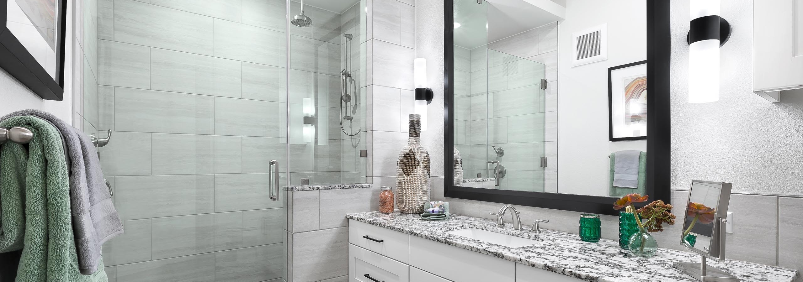 Interior view of AMLI Lakeline bathroom with white cabinetry with large mirror above and a tile and glass walk in shower with
