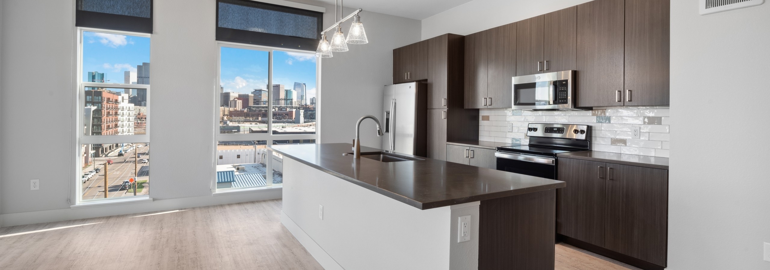 Kitchen with city skyline with large island and dark woodgrain cabinets and light wood flooring at AMLI RiNo apartments