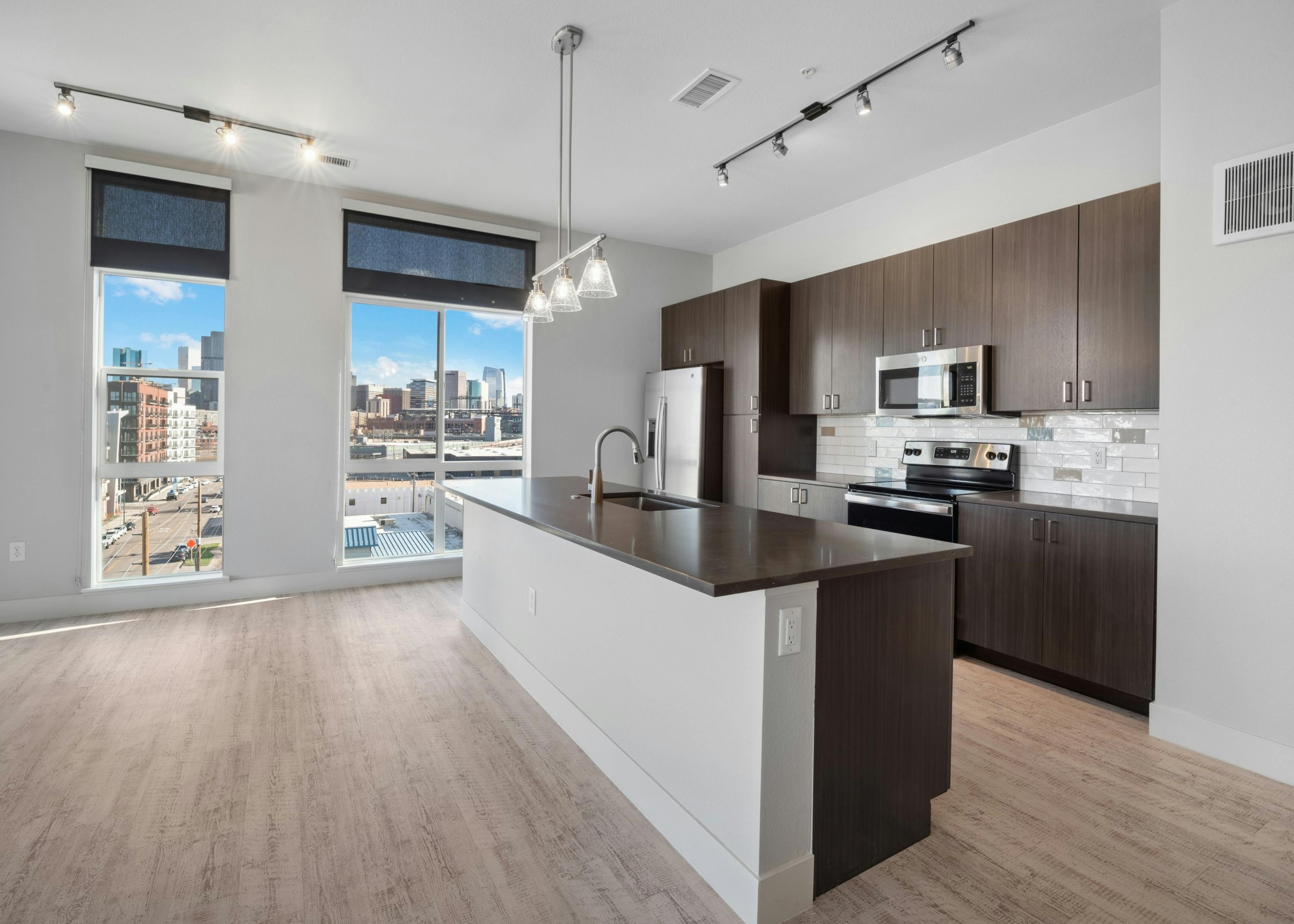 Kitchen with city skyline with large island and dark woodgrain cabinets and light wood flooring at AMLI RiNo apartments