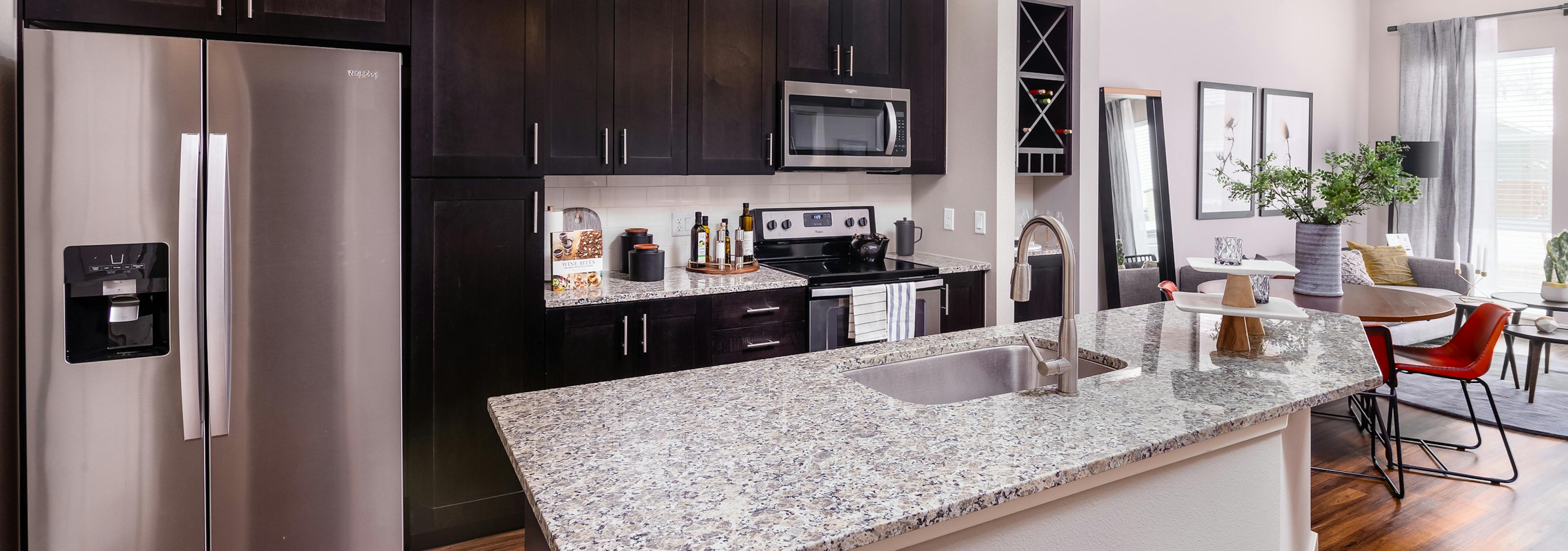 AMLI Littleton Village apartment kitchen with sink on island, dark cabinets and tile backsplash facing round dining table