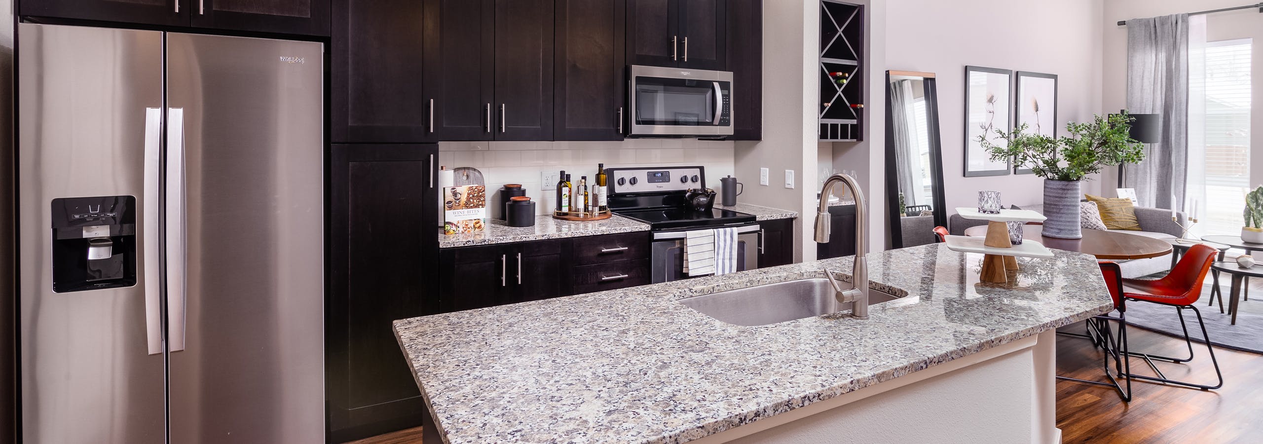 AMLI Littleton Village apartment kitchen with sink on island, dark cabinets and tile backsplash facing round dining table
