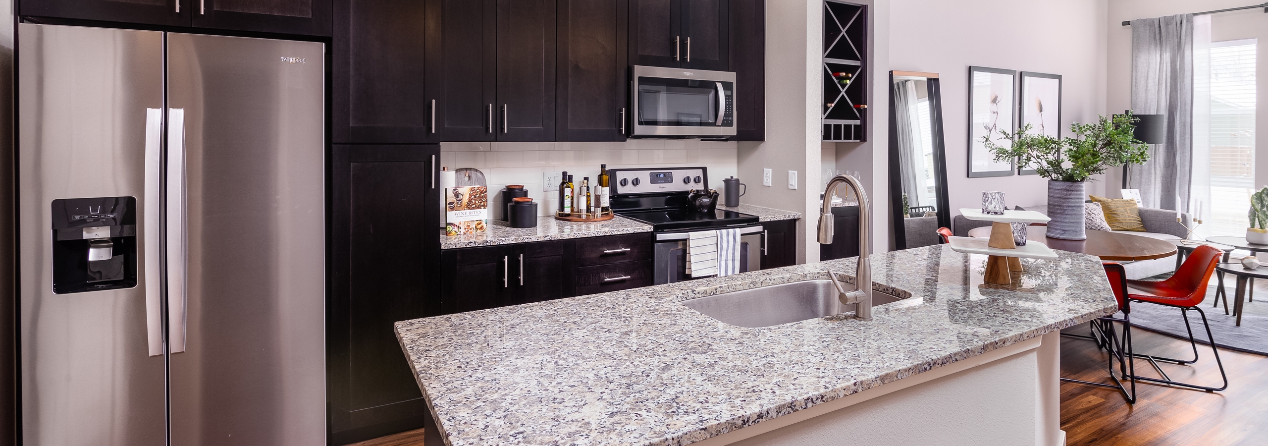 AMLI Littleton Village apartment kitchen with sink on island, dark cabinets and tile backsplash facing round dining table