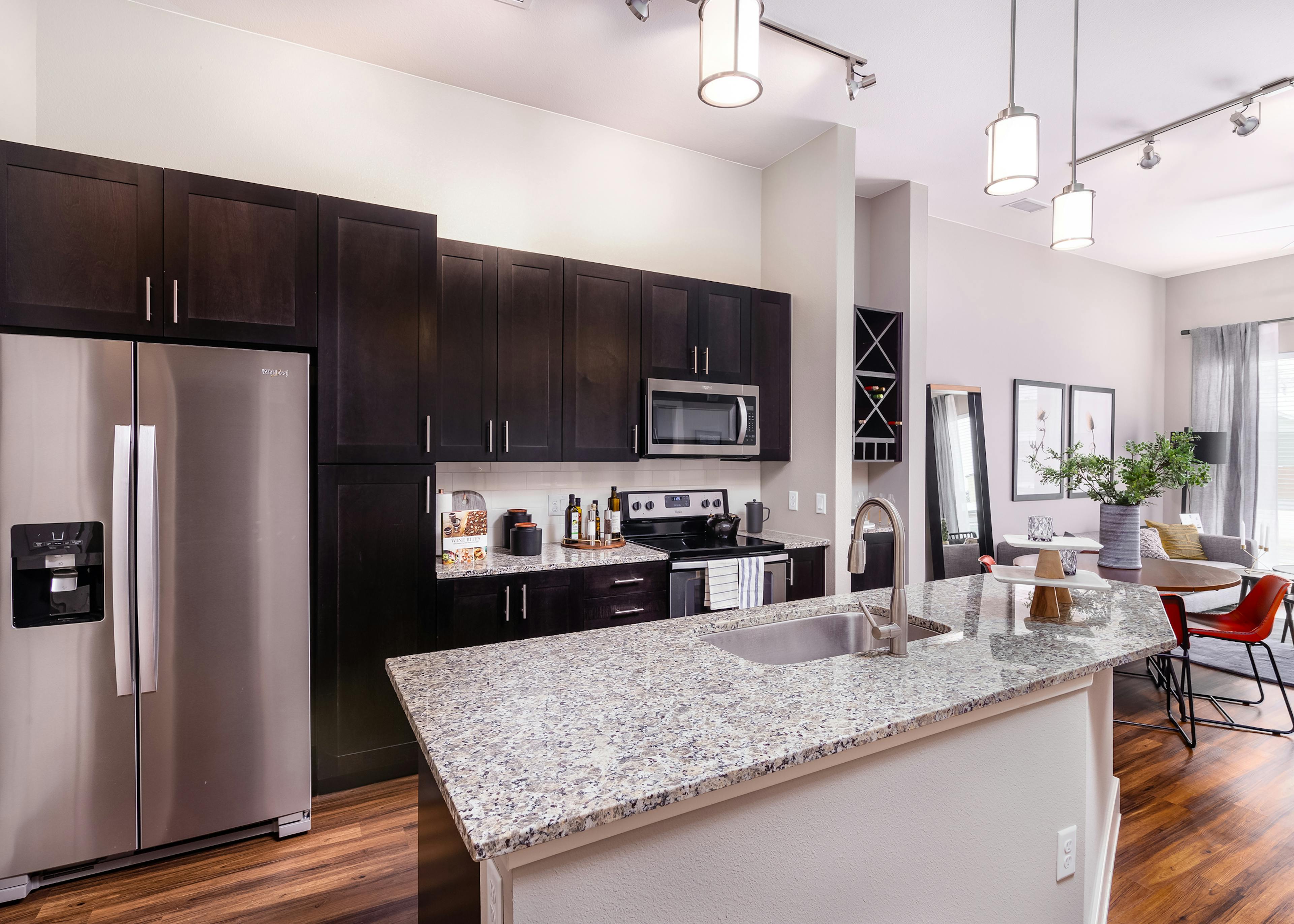 AMLI Littleton Village apartment kitchen with sink on island, dark cabinets and tile backsplash facing round dining table