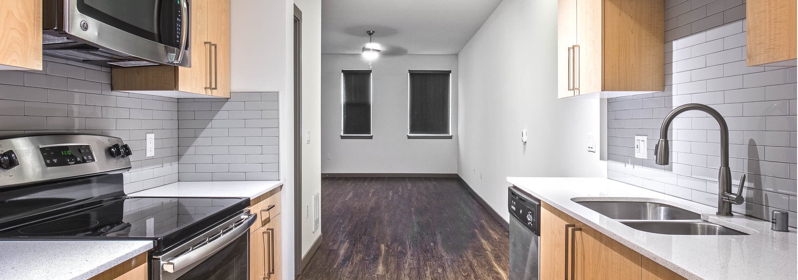 Interior view of AMLI Mark24 apartment kitchen with light cabinets light back splash white quartz counter tops and stainless steel appliances and view of living room