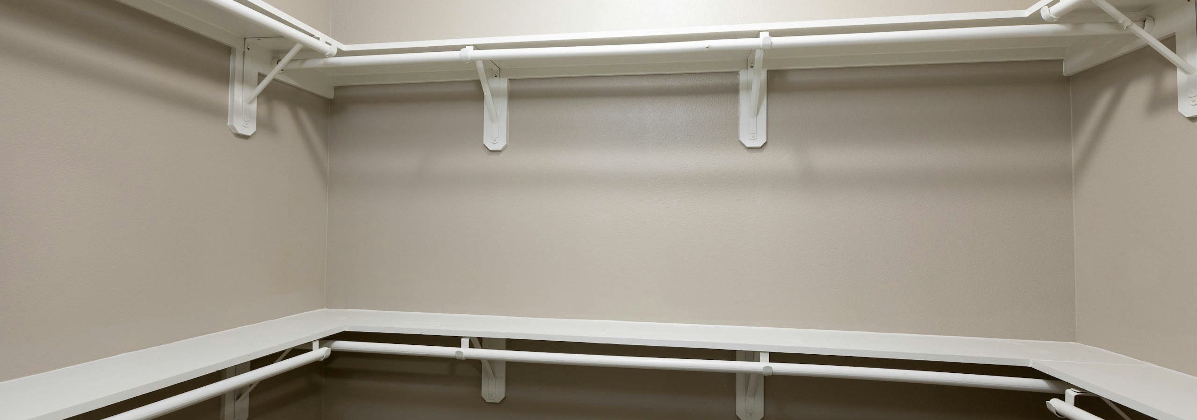 Close up view of spacious walk in closet at AMLI Eastside apartment community with white built in shelving and light walls