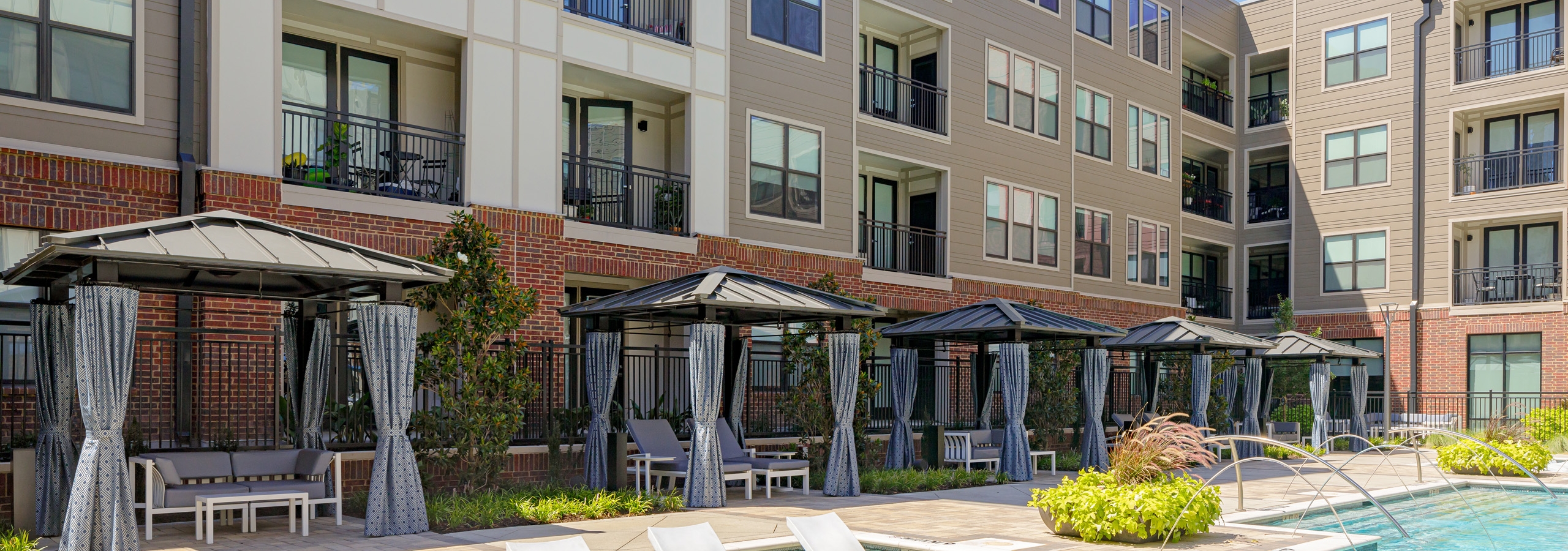 Day view of AMLI Addison poolside cabanas with building behind them and  lush landscape and in water lounge seating