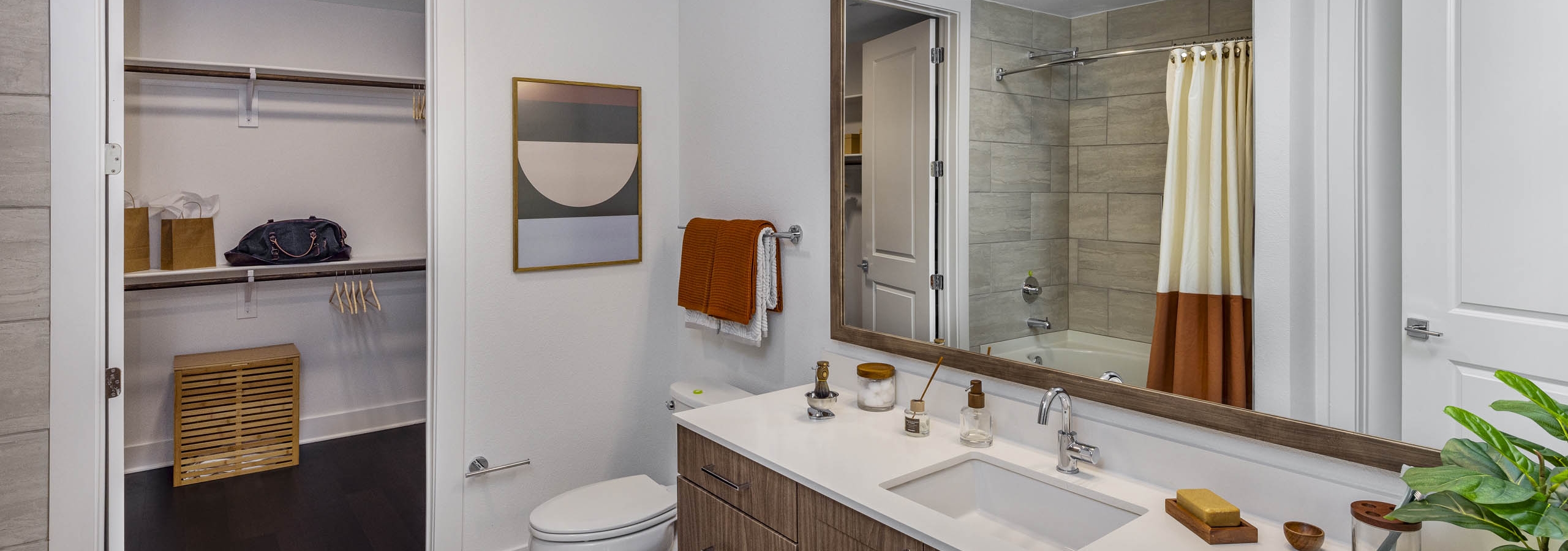 AMLI Branch Park bathroom with white quartz countertop and sink with wood cabinets and large mirror with view into closet