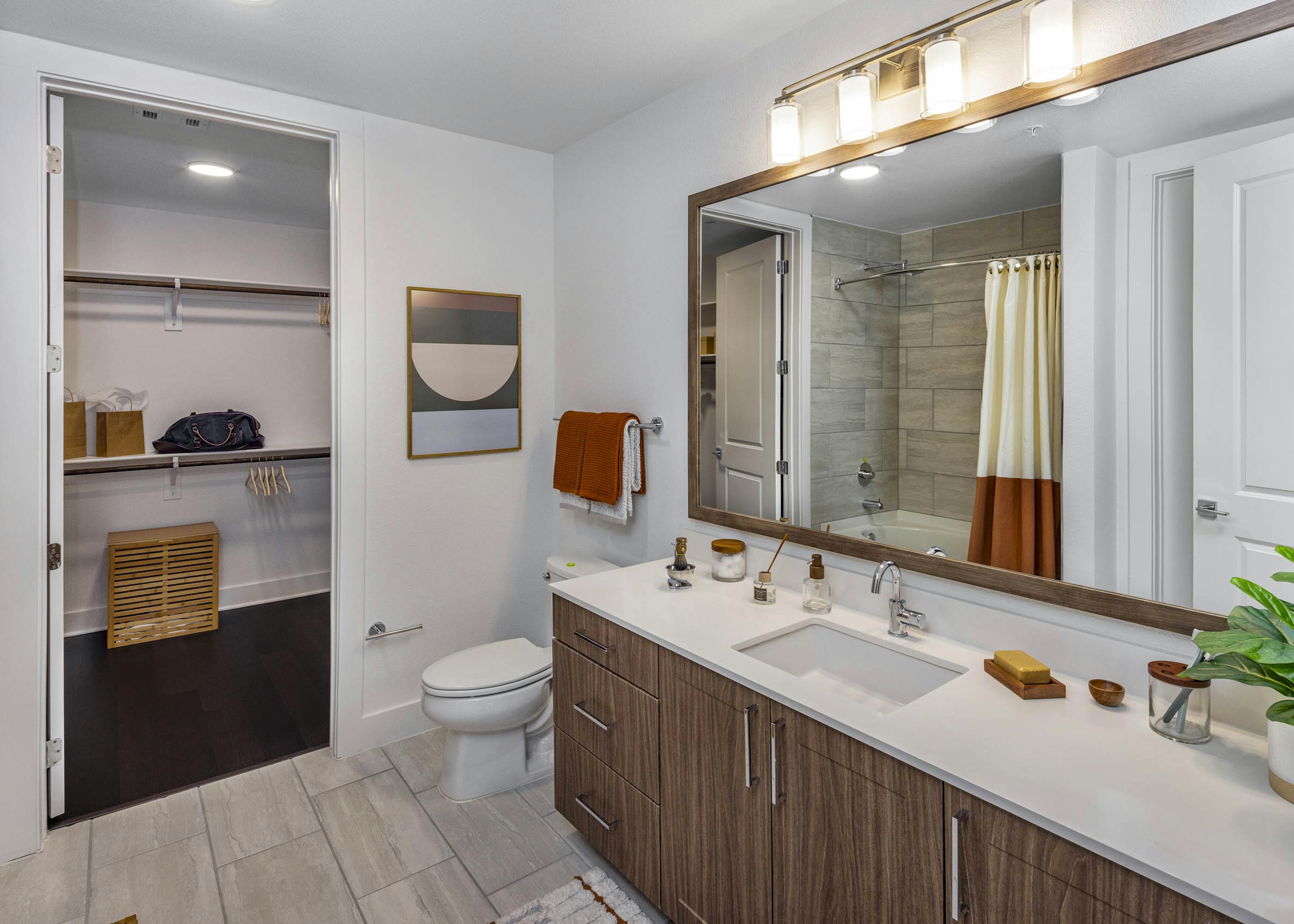 AMLI Branch Park bathroom with white quartz countertop and sink with wood cabinets and large mirror with view into closet