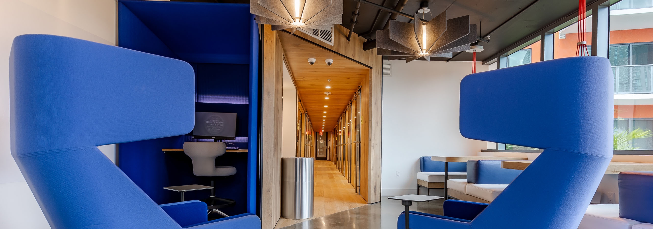 Interior view of AMLI Midtown Miami coworking space with blue modern armchairs and built in desks and view of long hallway