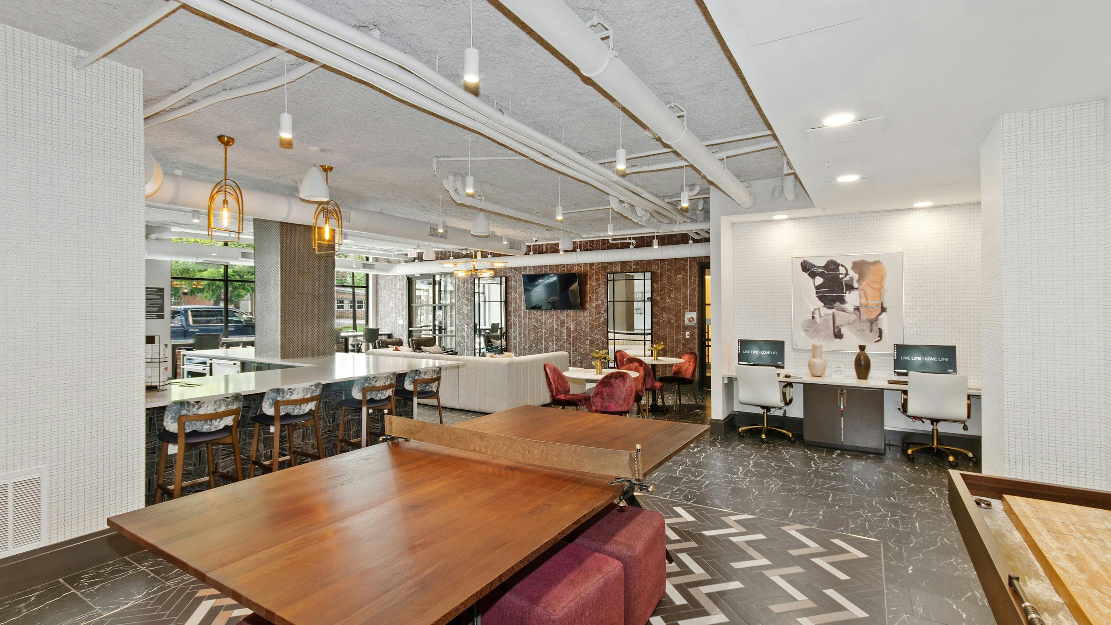Play area at AMLI Quadrangle resident area featuring a wooden table for tennis and a shuffle board surrounded by red ottomans