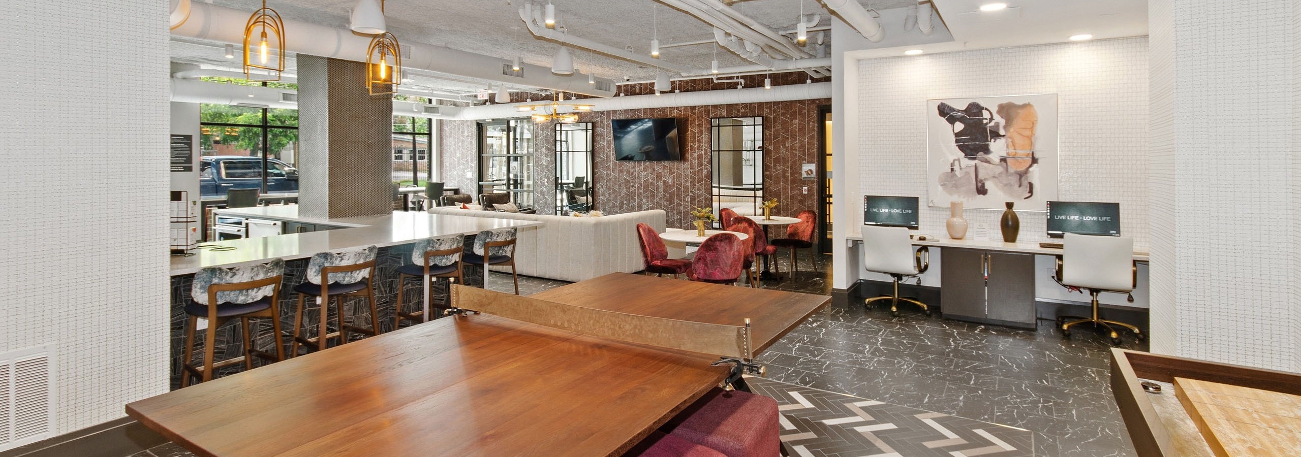Play area at AMLI Quadrangle resident area featuring a wooden table for tennis and a shuffle board surrounded by red ottomans