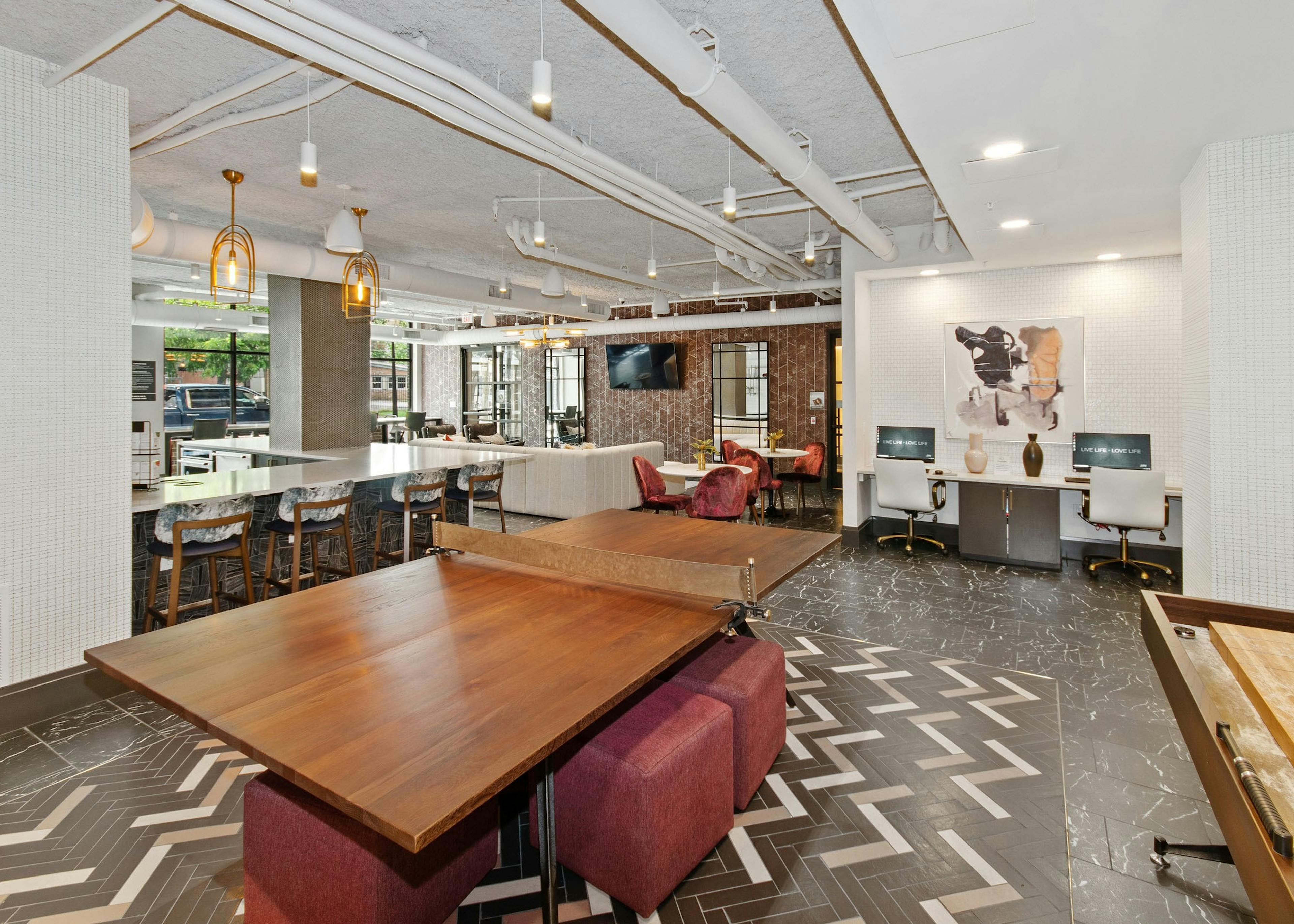 Play area at AMLI Quadrangle resident area featuring a wooden table for tennis and a shuffle board surrounded by red ottomans