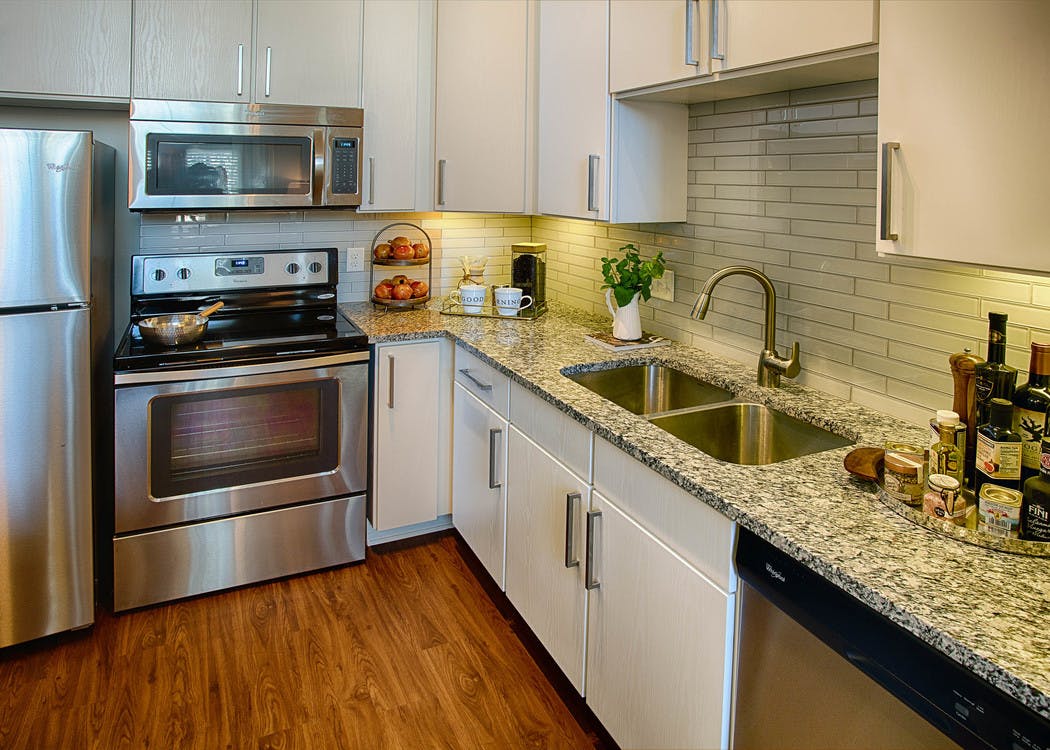 A kitchen at AMLI Denargo Market apartments with a tile back splash with white cupboards and an oven with overhead microwave