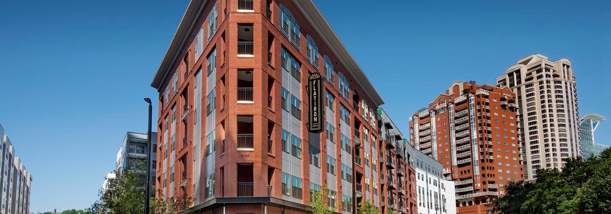 AMLI Flatiron apartment building exterior with red brick facade set on tree lined street corner with parked cars