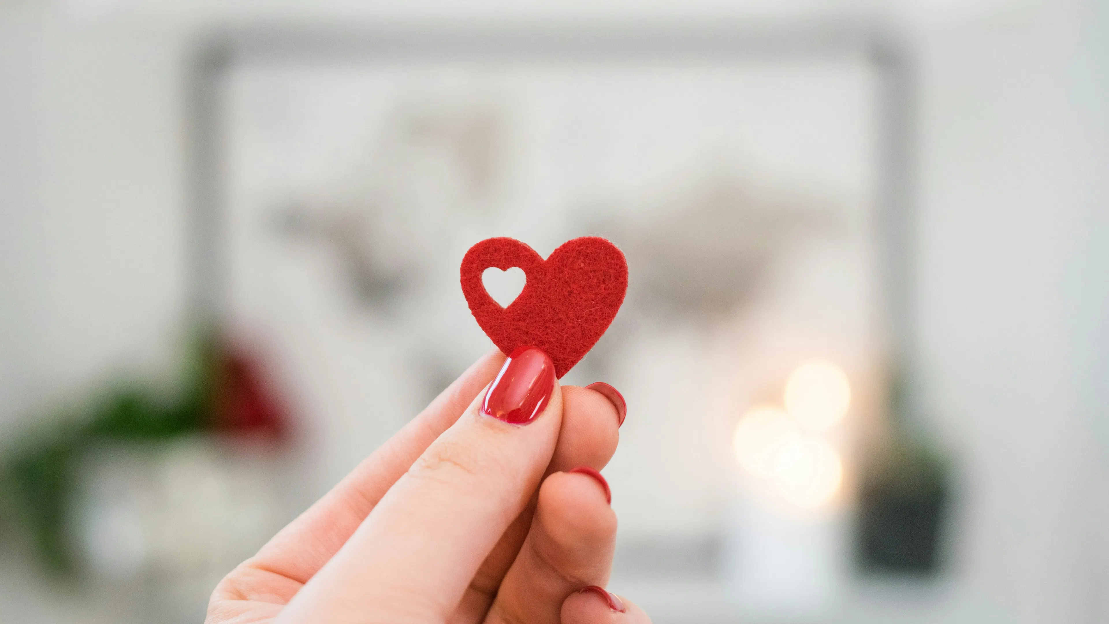 A woman's fingers with red painted nails holding a red cutout heart