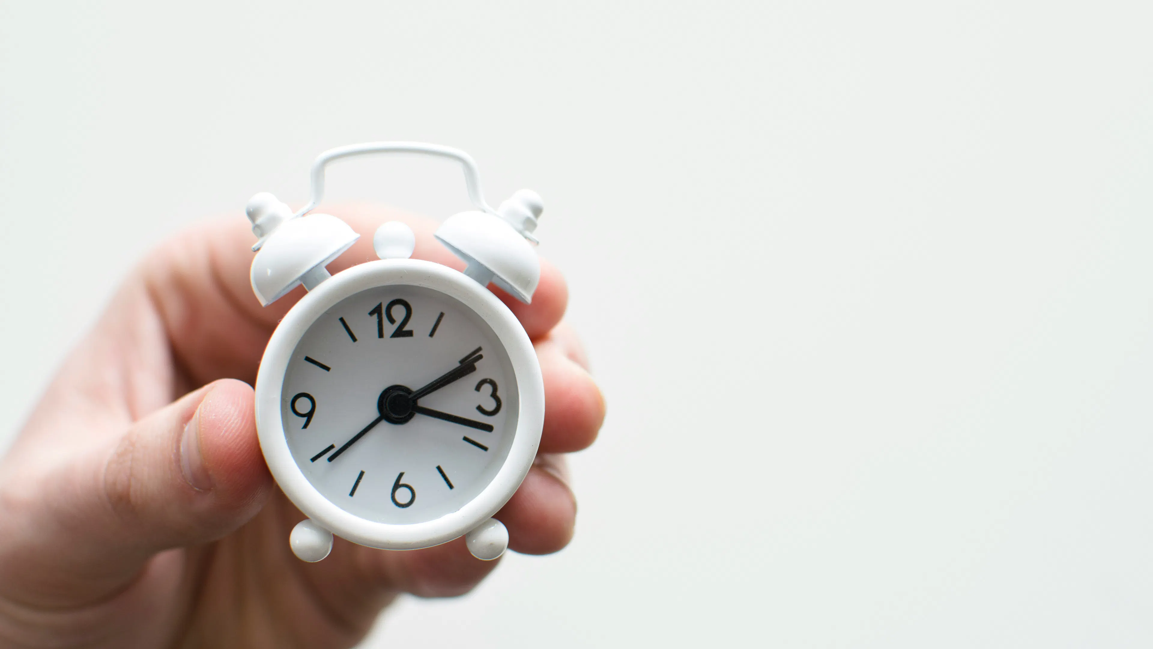 A person's hand holding a small white alarm clock figurine