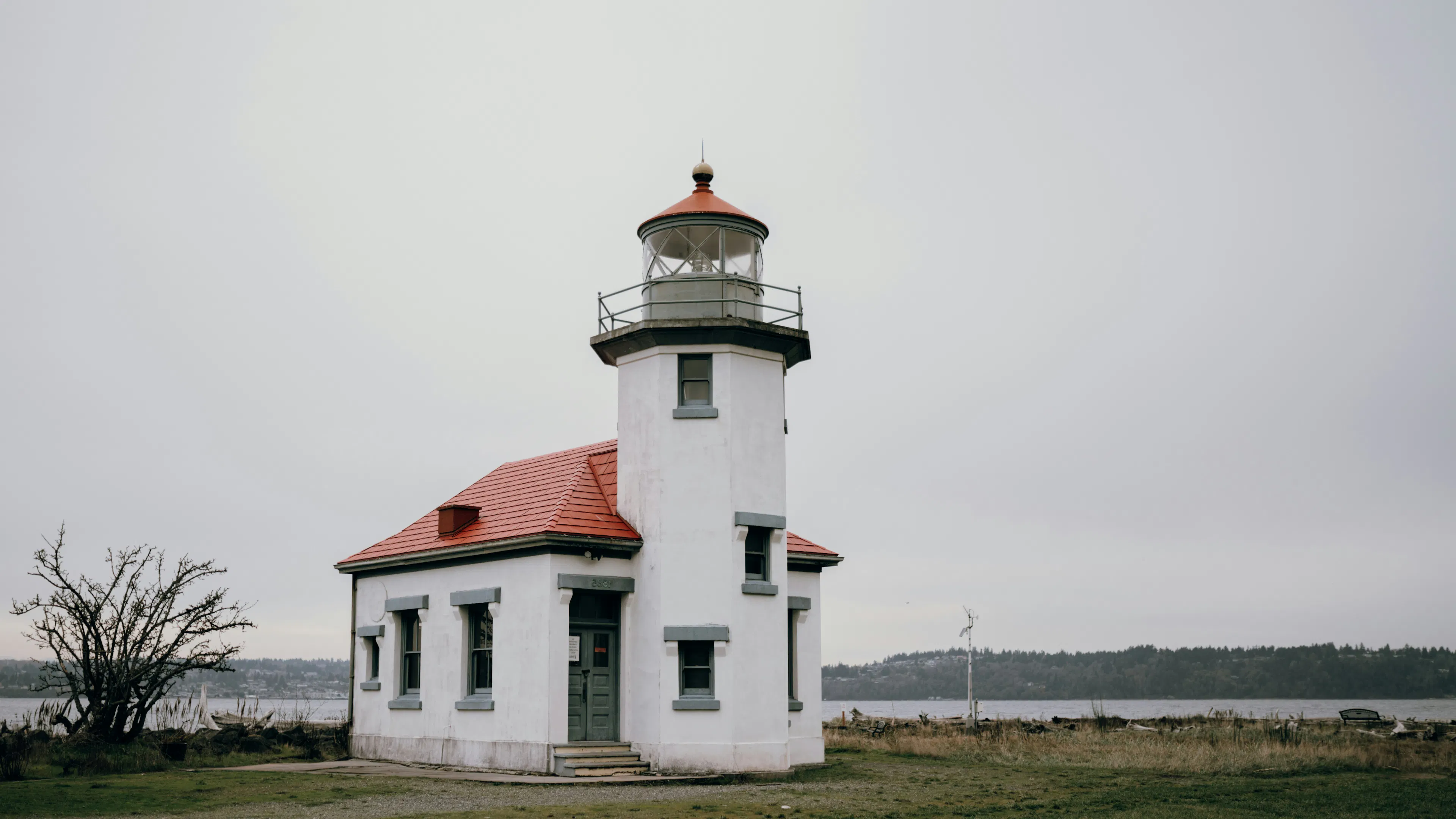 A small lighthouse with white walls and a red roof located next to a calm shore