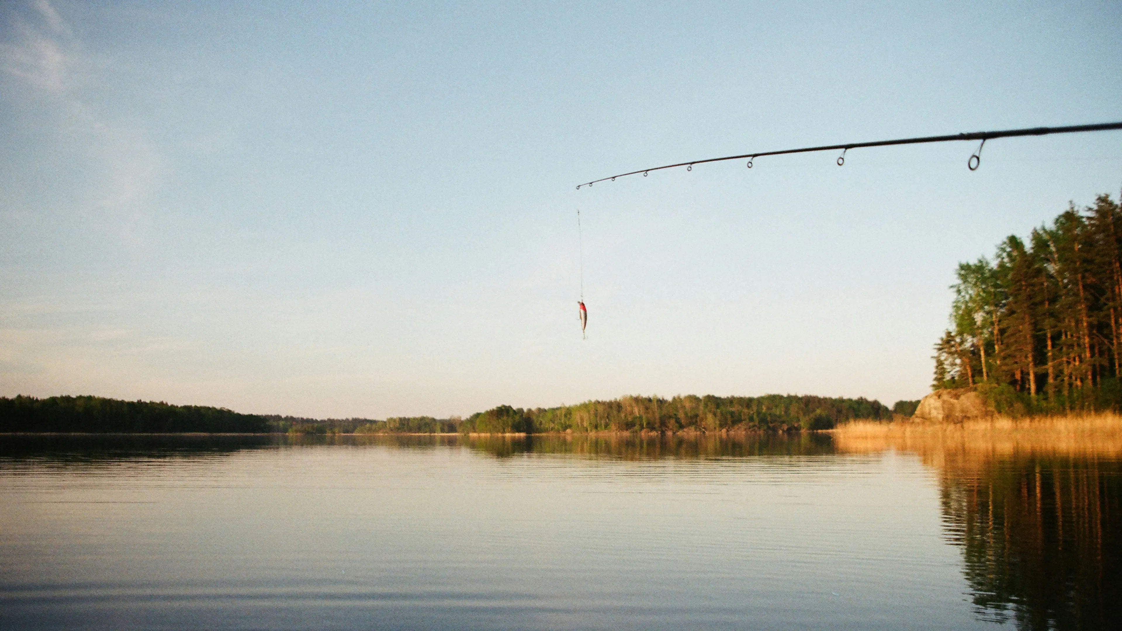 A fishing rod with a small lure with a large peaceful lake in the background
