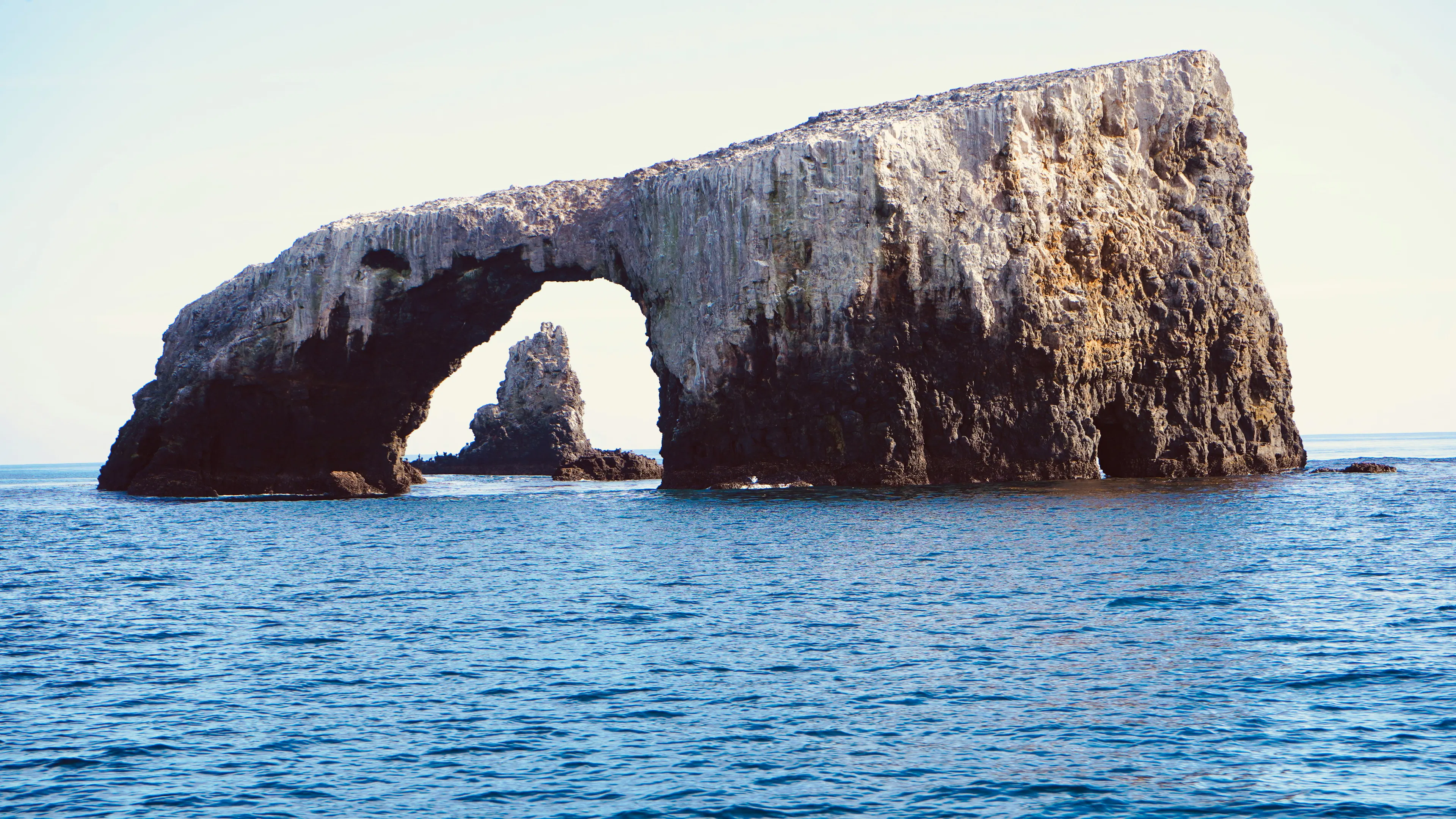 A stone arch in the sea with another rocky island seen through the archway