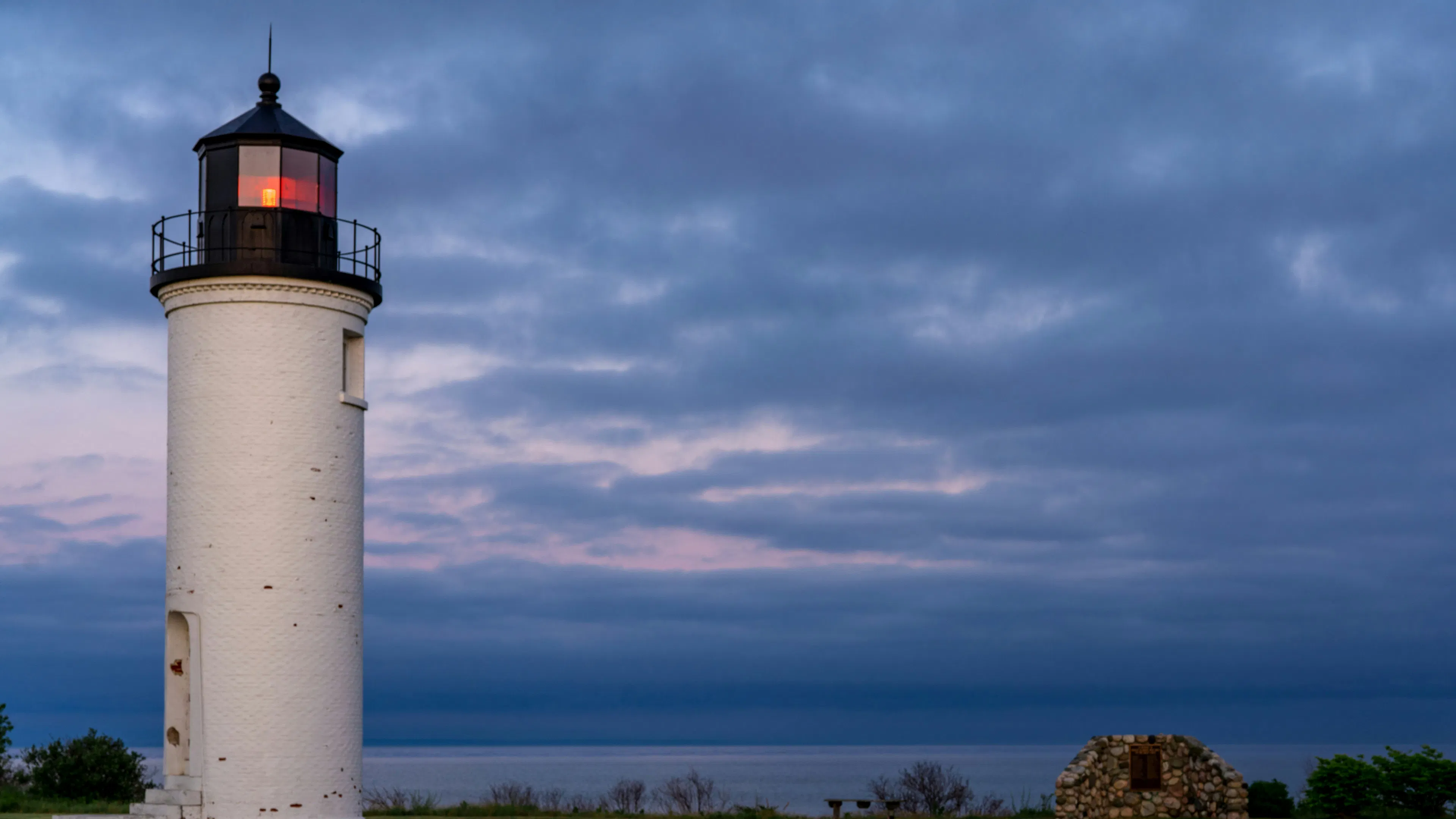 A white lighthouse with a black top located on the tip of a flat, forested island in the middle of a large lake