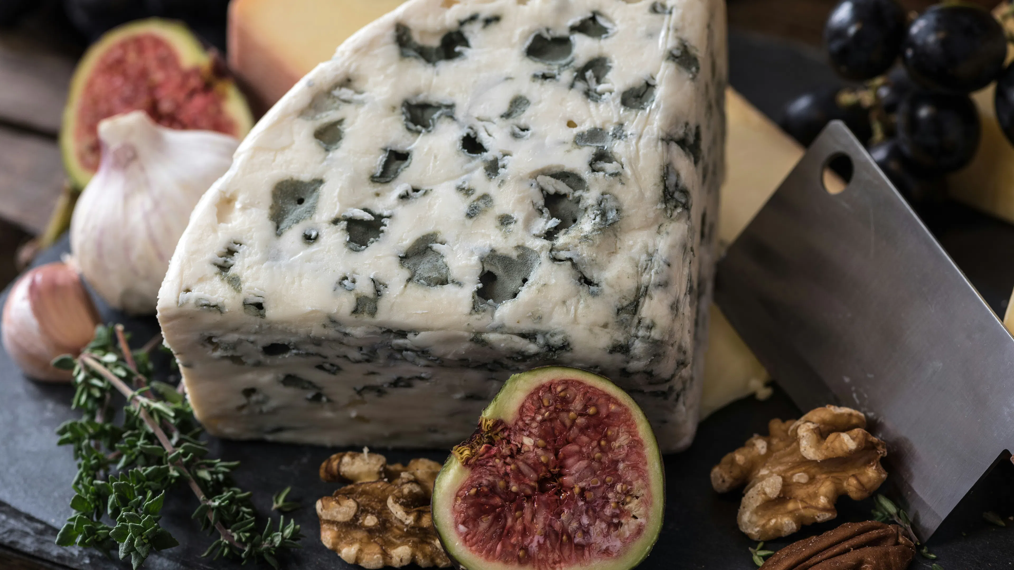 A large slice of goat cheese flavored with herbs on a plate beside sliced figs and walnuts