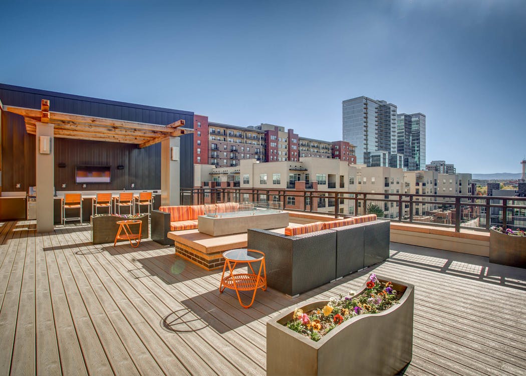 Exterior view of the rooftop deck at AMLI Riverfront Park with fire pit and several seating areas and view of Denver skyline