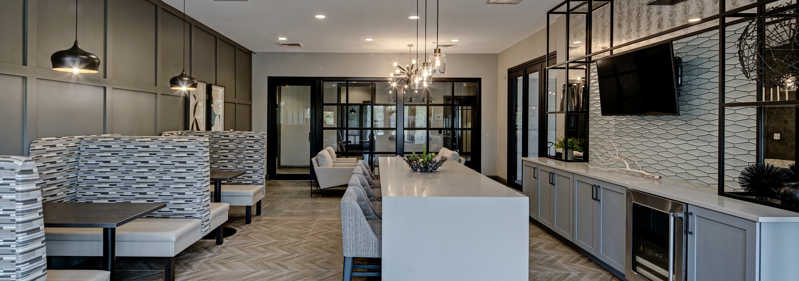 Resident lounge at AMLI at Seven Bridges apartments with white serving bar with stools facing mounted TV and booth seating