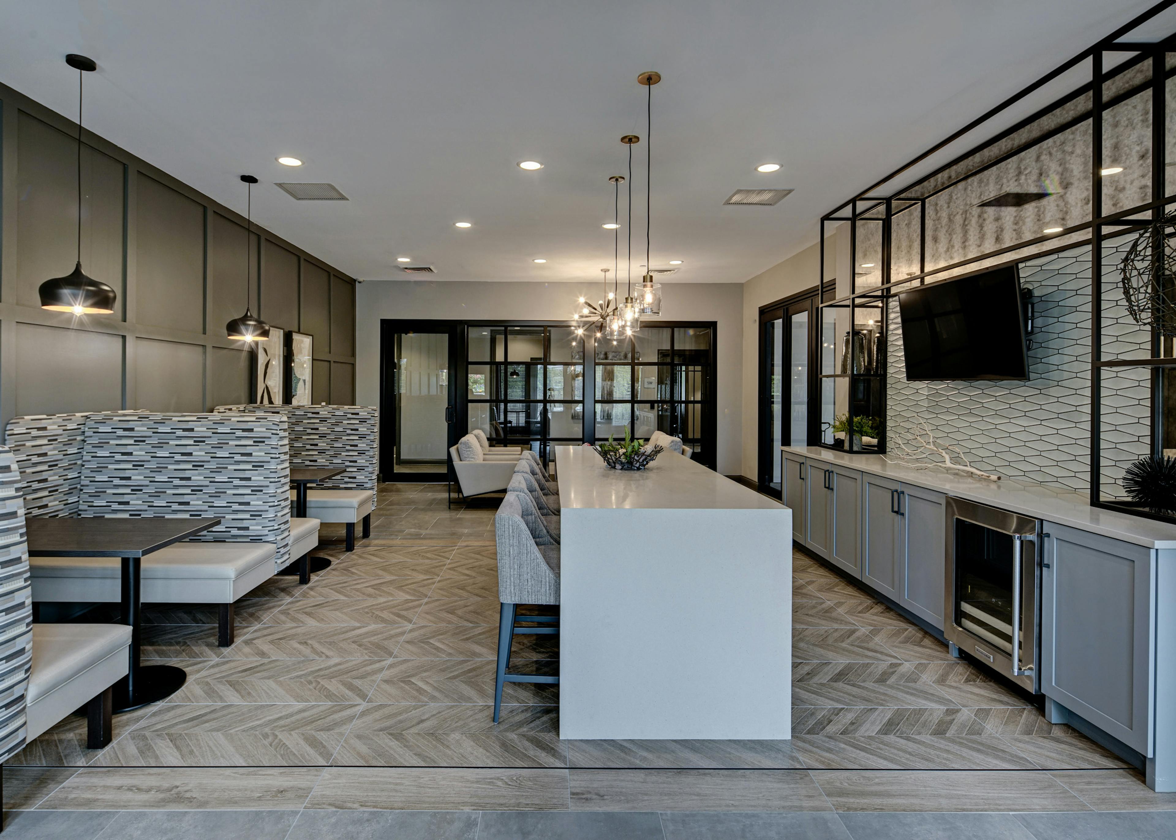 Resident lounge at AMLI at Seven Bridges apartments with white serving bar with stools facing mounted TV and booth seating