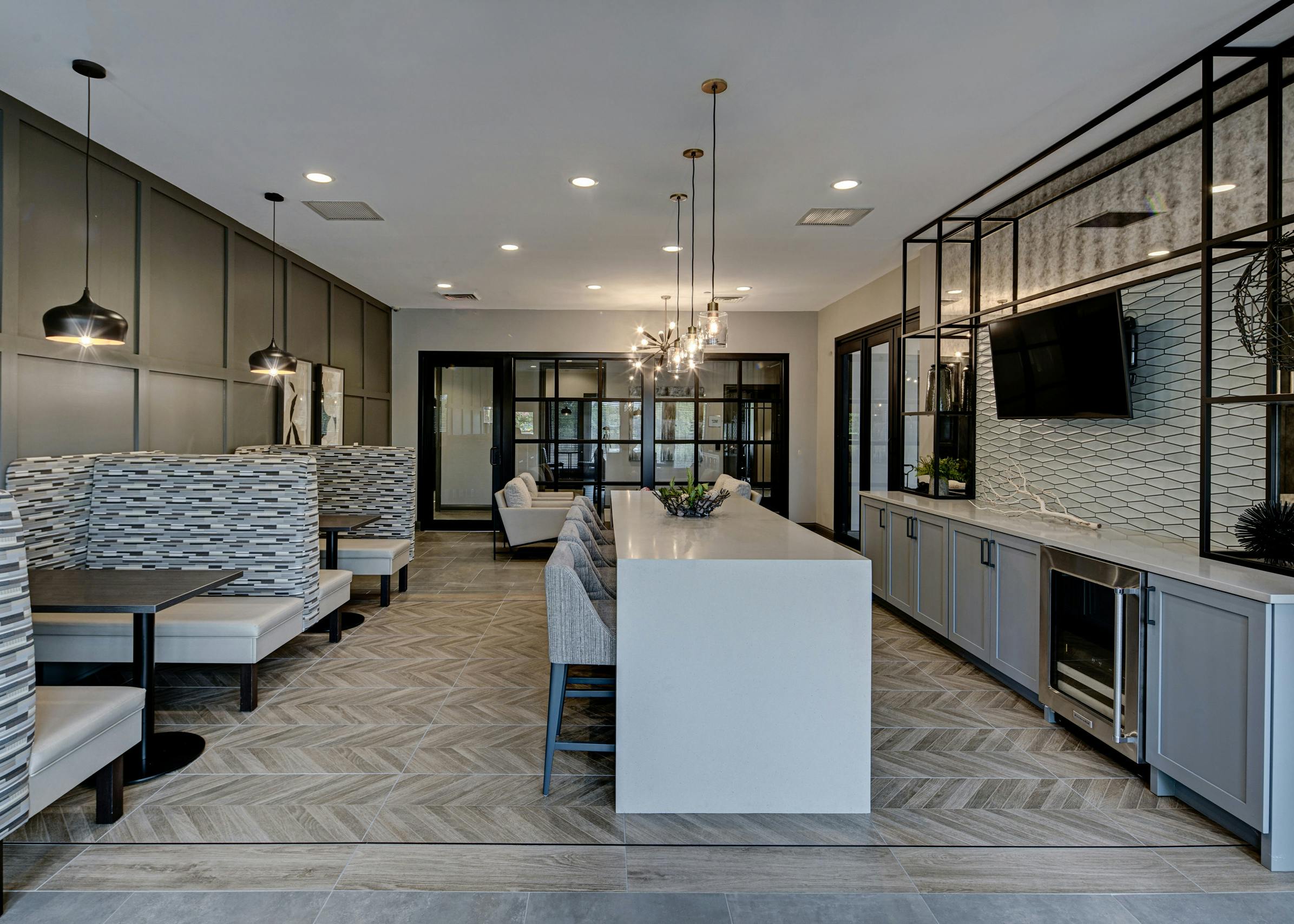 Resident lounge at AMLI at Seven Bridges apartments with white serving bar with stools facing mounted TV and booth seating