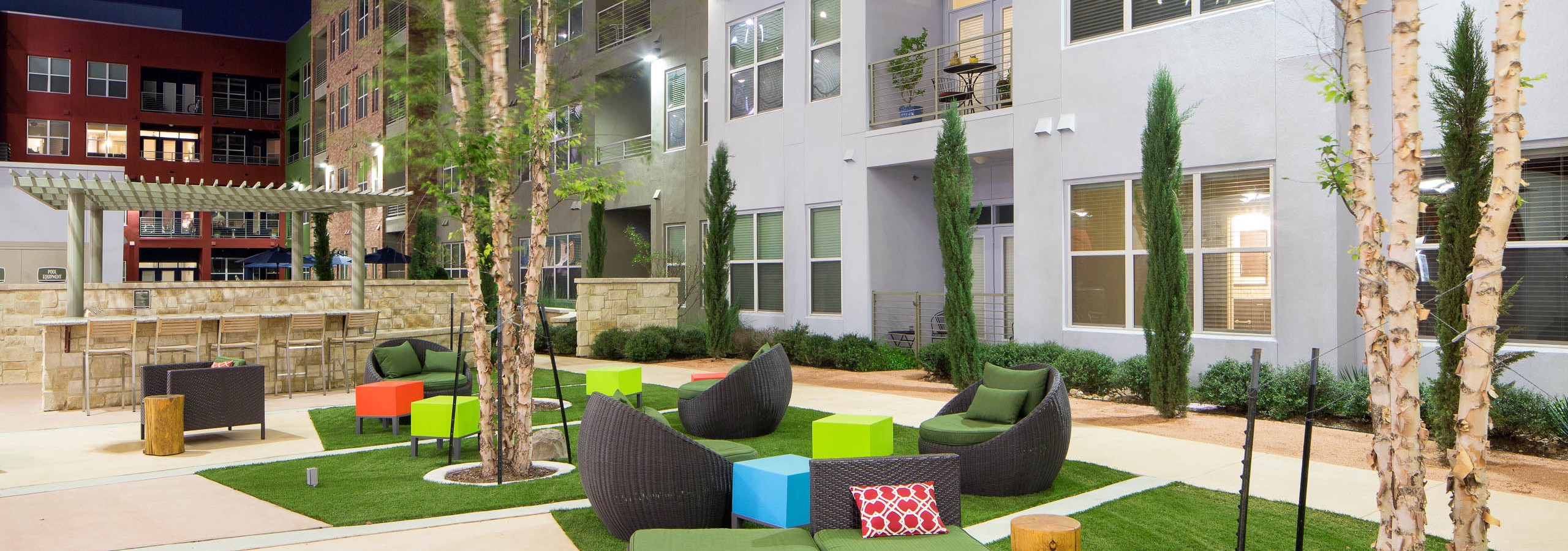 Daytime view of AMLI at Mueller courtyard with black lounge chairs and colorful foot rests on squares of grass in the center
