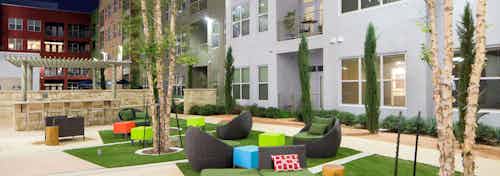 Daytime view of AMLI at Mueller courtyard with black lounge chairs and colorful foot rests on squares of grass in the center